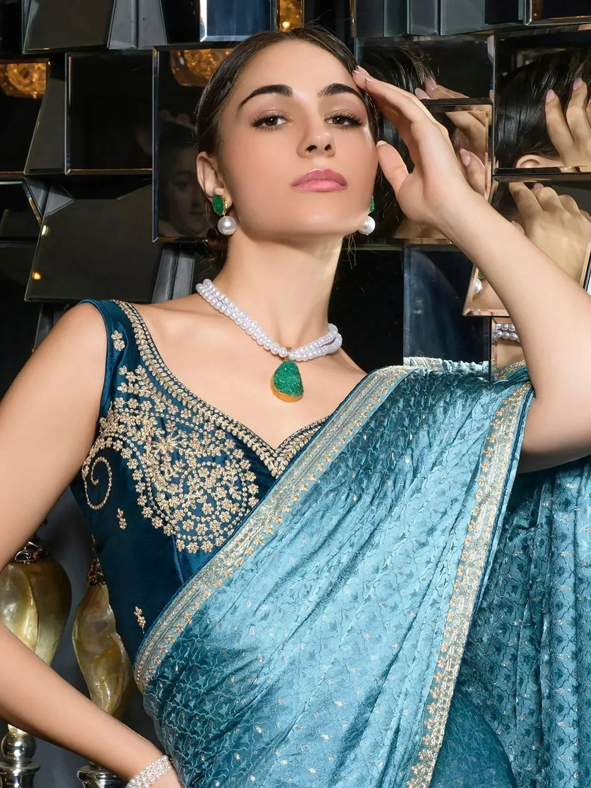 Teal velvet saree with gold embroidery, pearl necklace, and green pendant for Indian ethnic wear