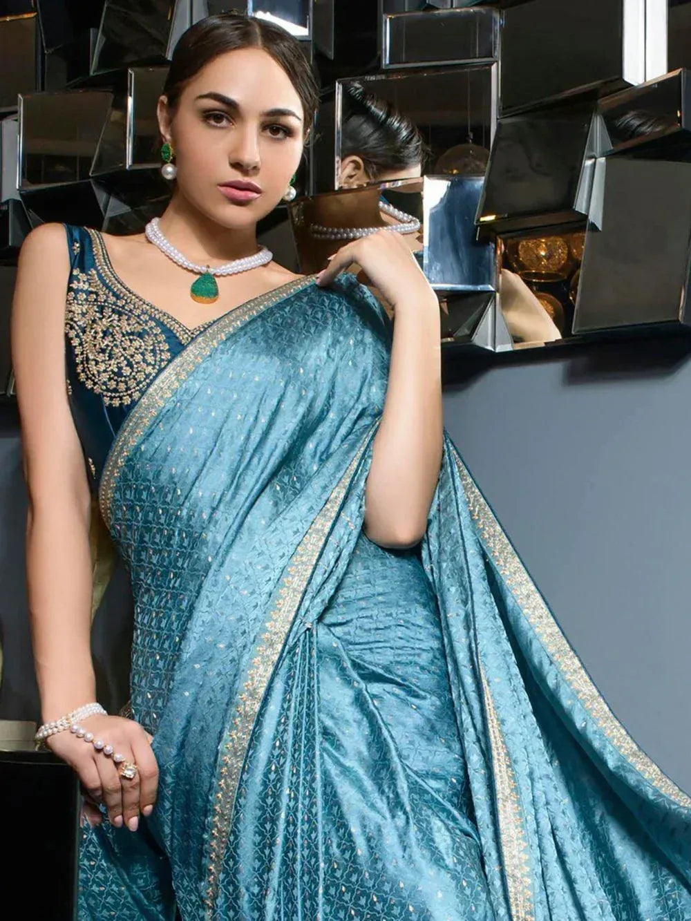 Teal designer saree with gold border and embellished blouse, styled with pearl jewelry for ethnic wear