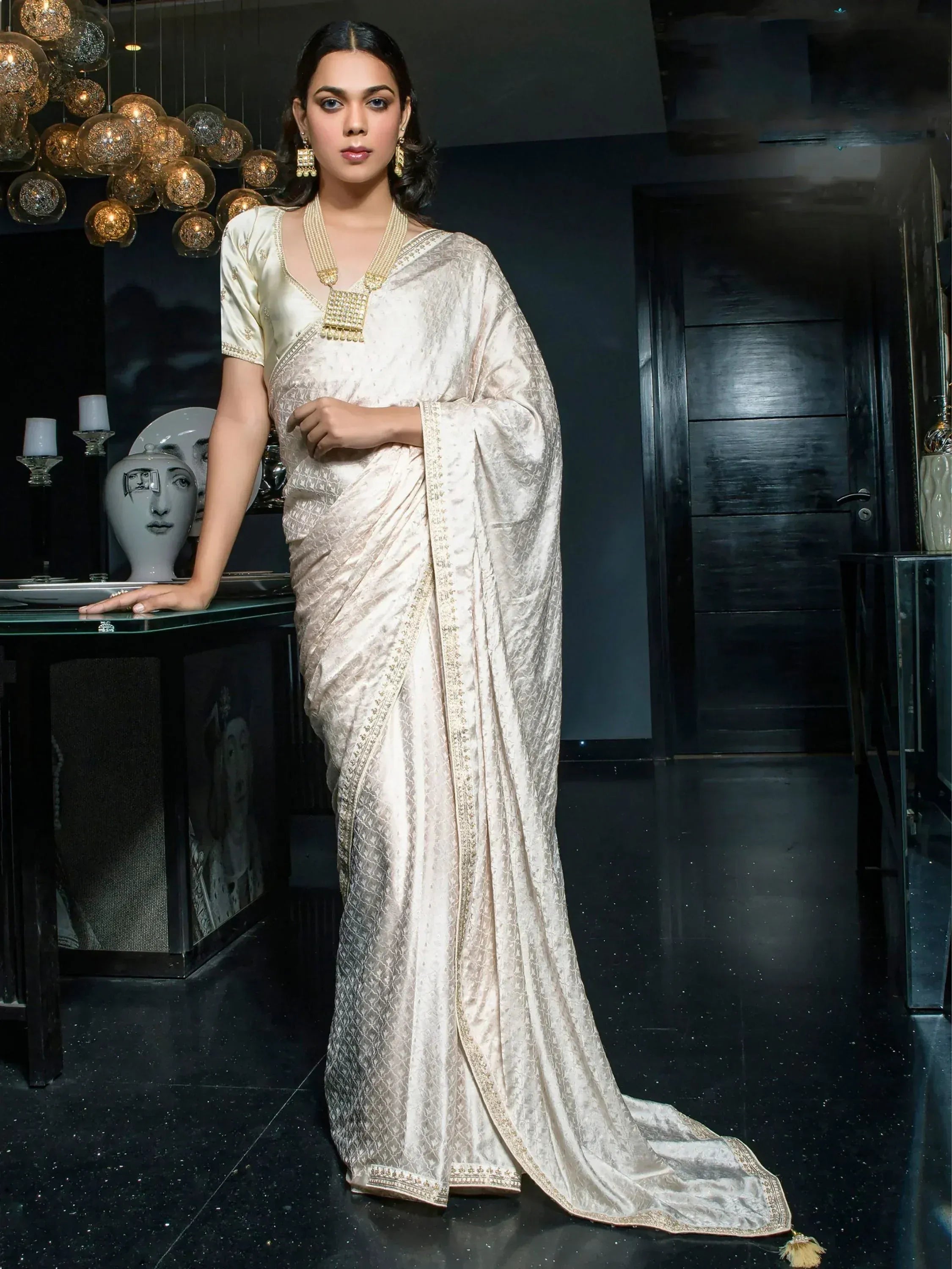 Elegant cream silk saree with gold embroidery, paired with matching blouse and traditional jewelry for festive occasions.