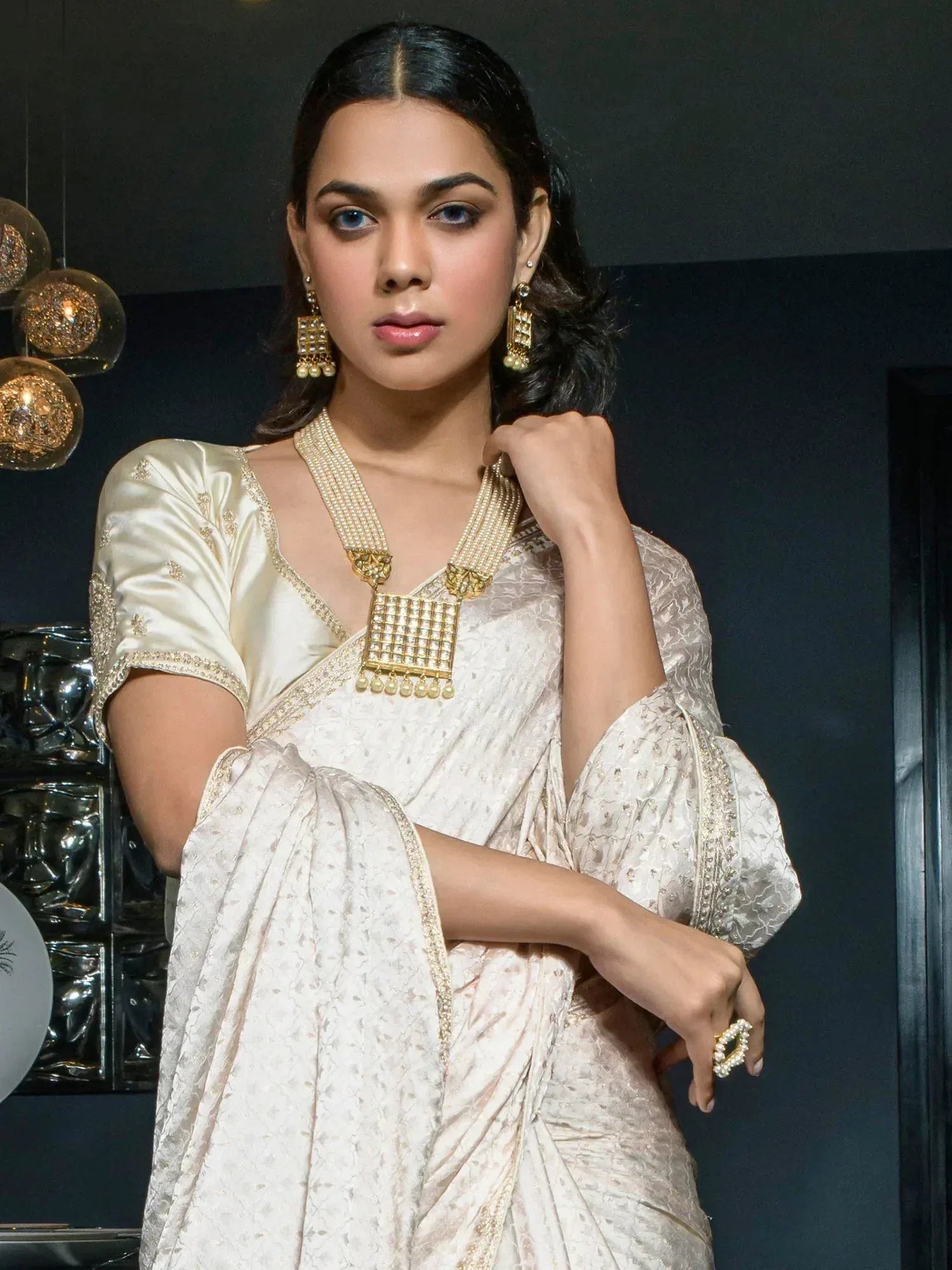 Elegant woman in cream embroidered saree with gold jewelry, showcasing Indian ethnic wear for festive occasions