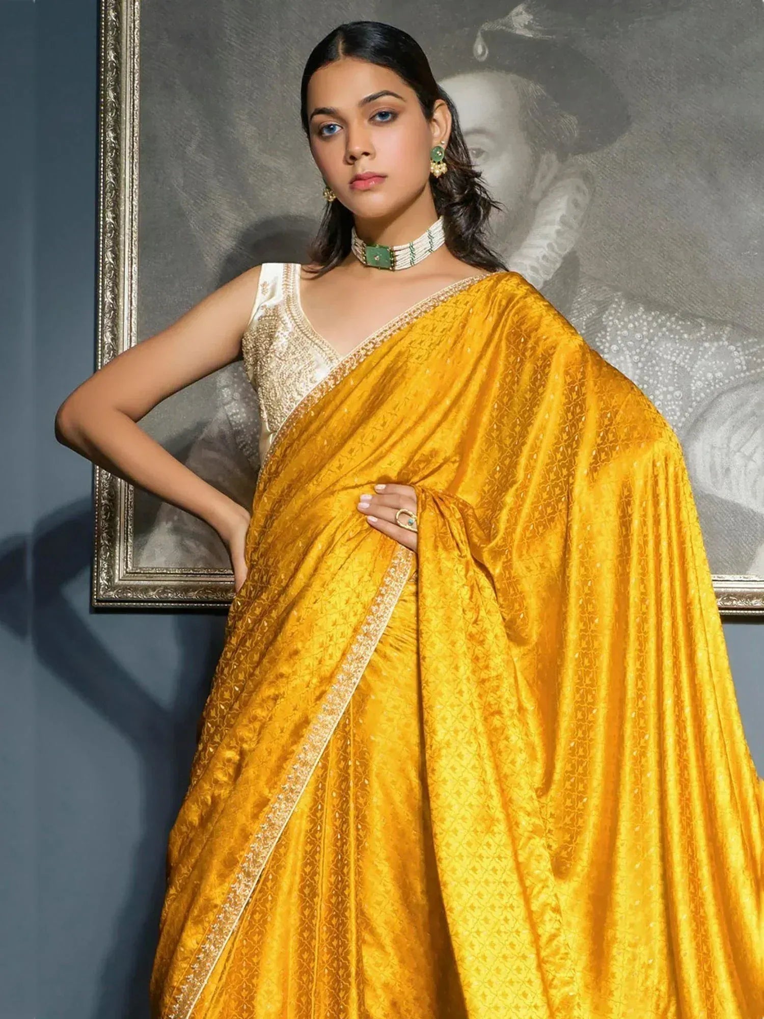 Yellow designer saree with gold embroidery, paired with white blouse and green jewelry, elegant ethnic wear