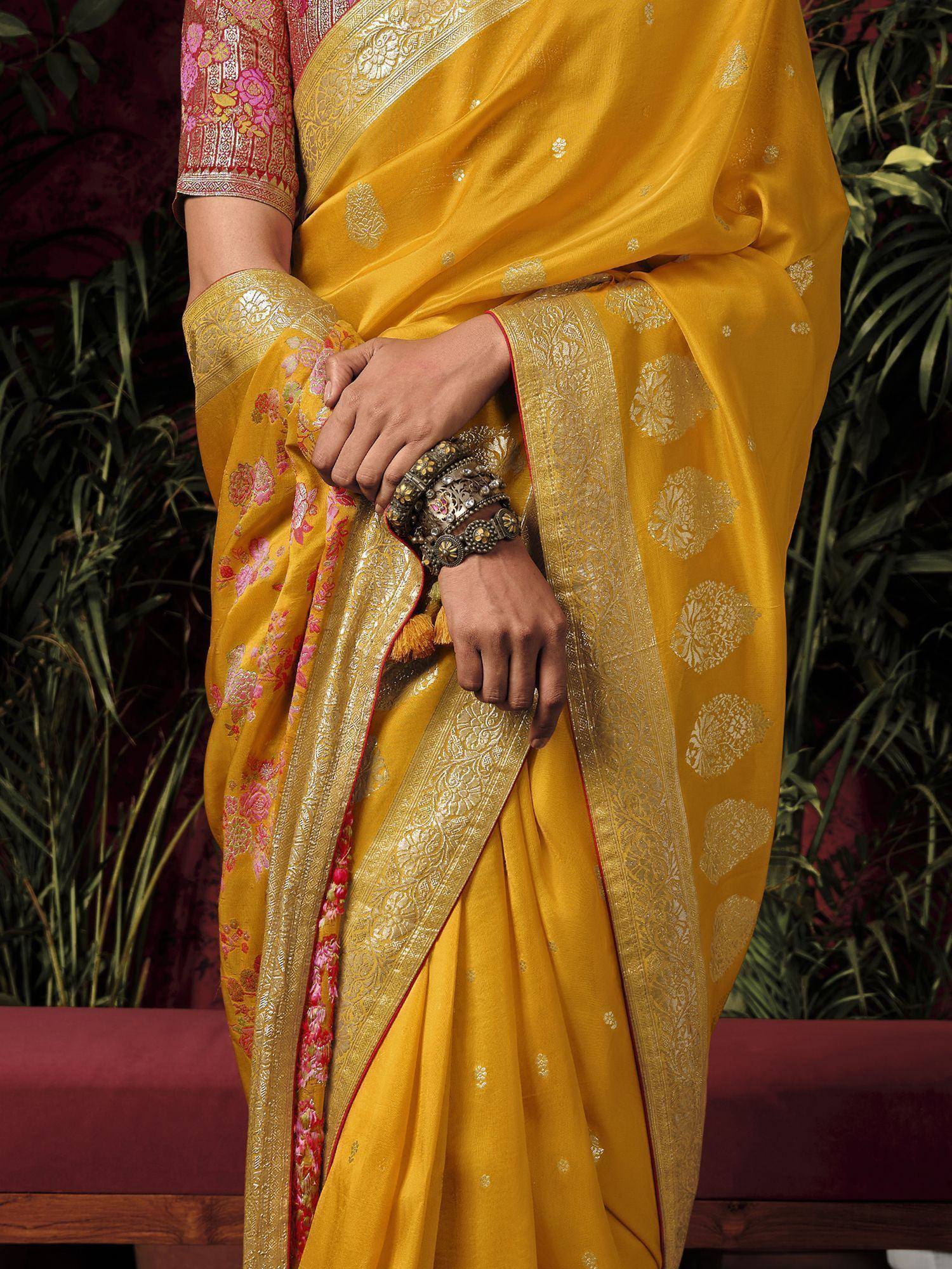 Yellow designer saree with gold floral motifs and pink border, paired with ornate bangles for ethnic wear