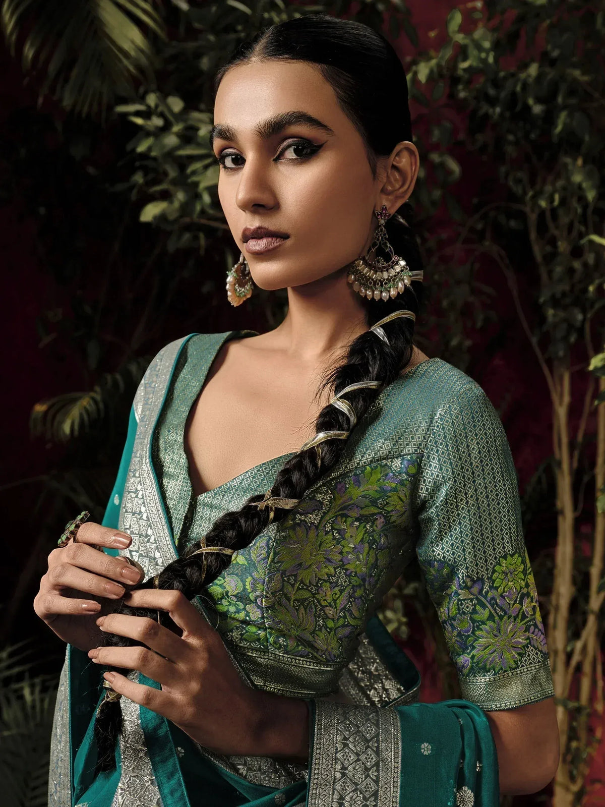 Elegant woman in teal floral saree with silver border, traditional Indian ethnic wear, styled with jhumka earrings and braided hair.