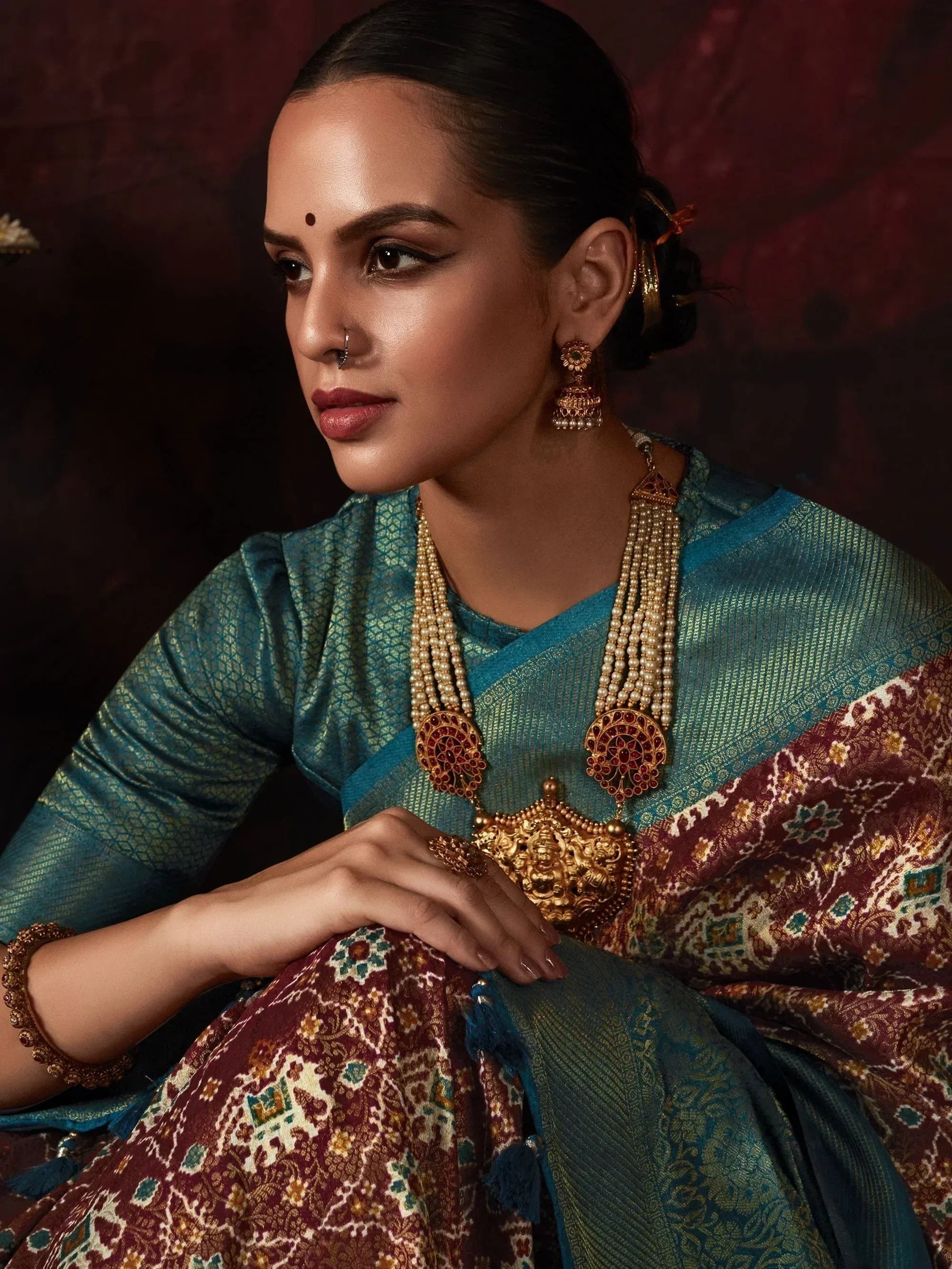 Elegant woman in teal and maroon ethnic saree with gold jewelry, perfect for Indian festive occasions.