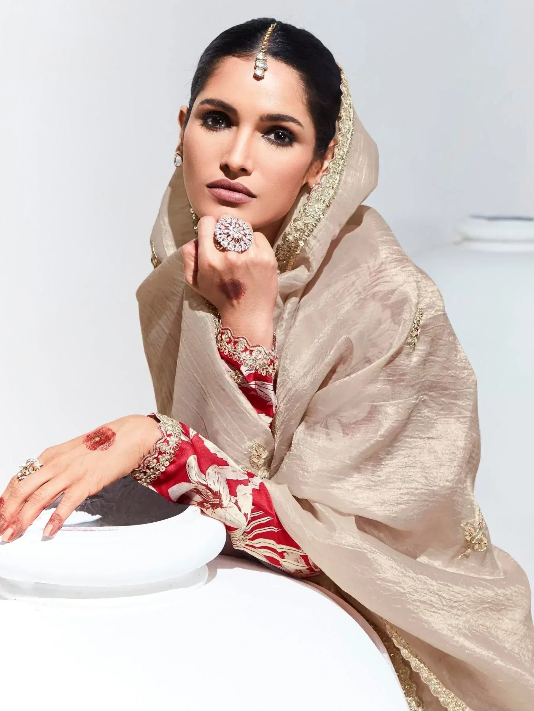 Elegant woman in red floral salwar kameez with beige dupatta, traditional Indian ethnic wear, adorned with jewelry and henna.