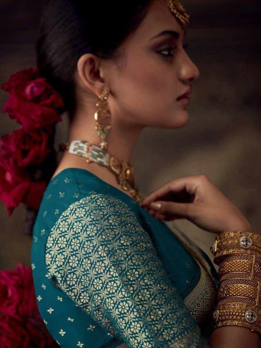 Woman in teal ethnic saree with gold embroidery, traditional jewelry, and red rose hair accessory