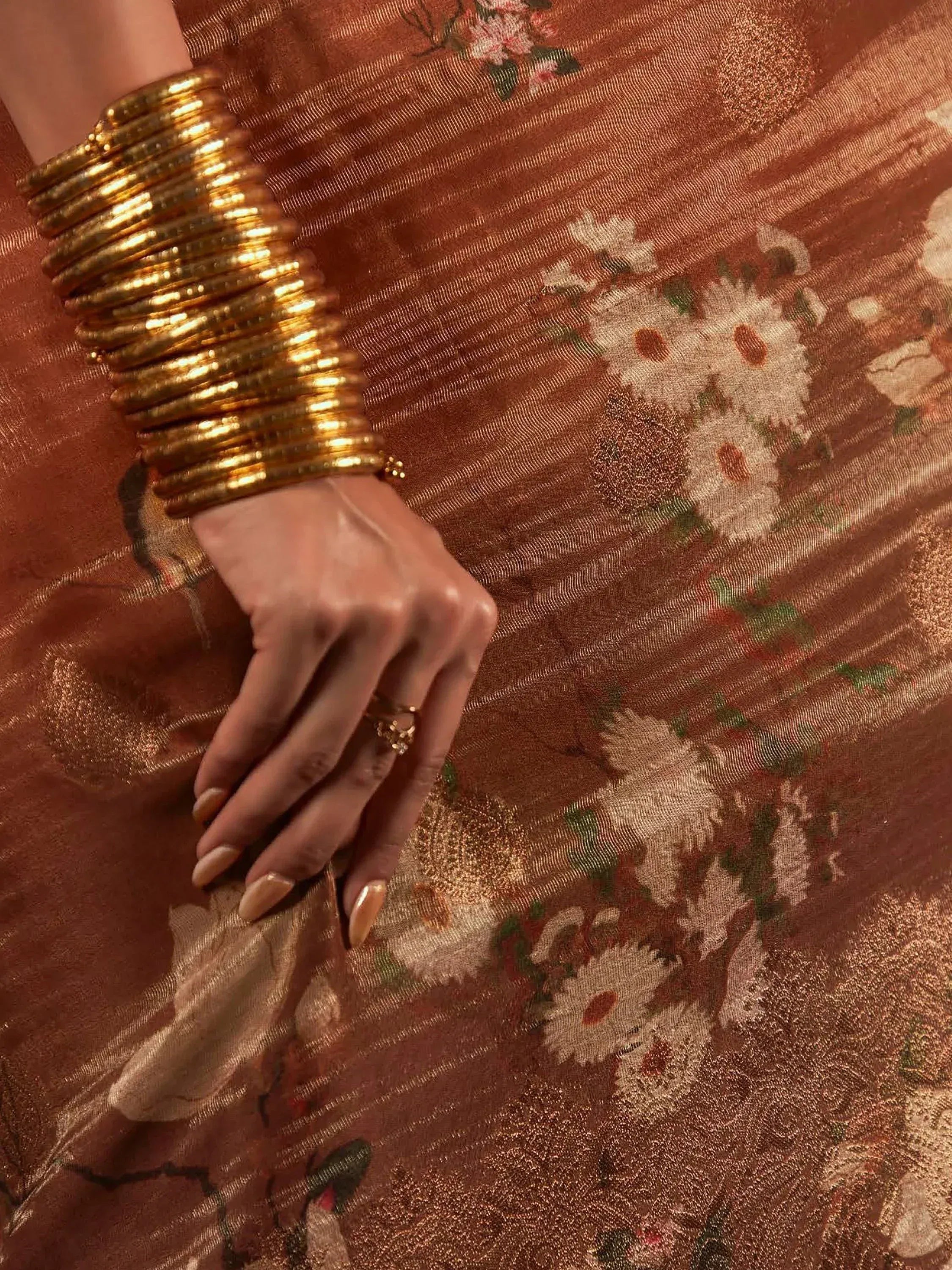 Golden bangles on hand over floral ethnic saree fabric, traditional Indian wear detail