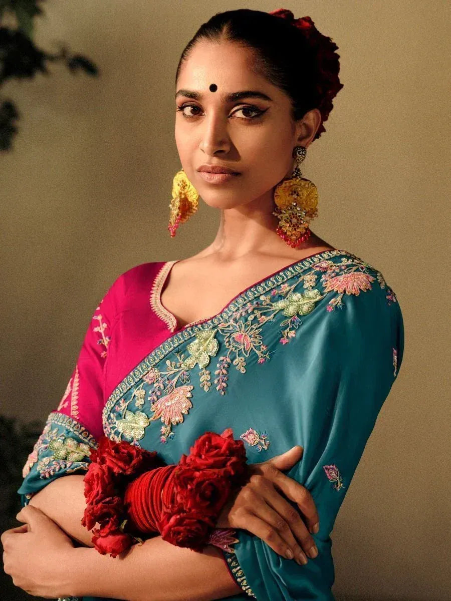 Woman in teal embroidered saree with pink blouse, floral hair accessory, and statement earrings