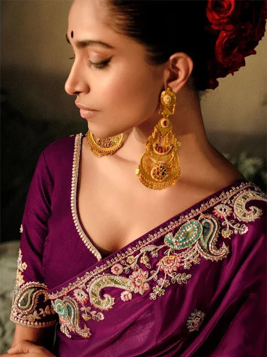 Woman in purple embroidered saree with gold jewelry and red rose hair accessory