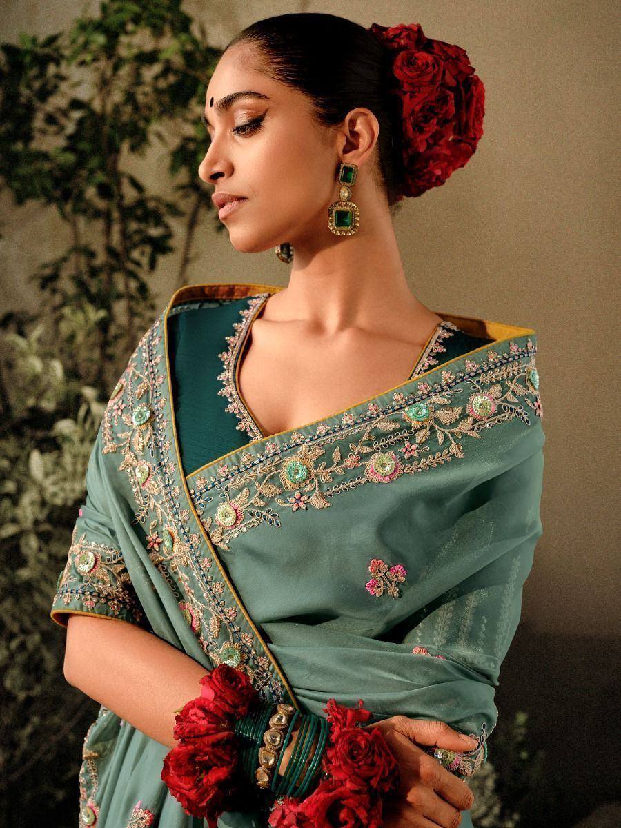 Elegant teal saree with floral embroidery, red rose hair accessory, and green statement earrings