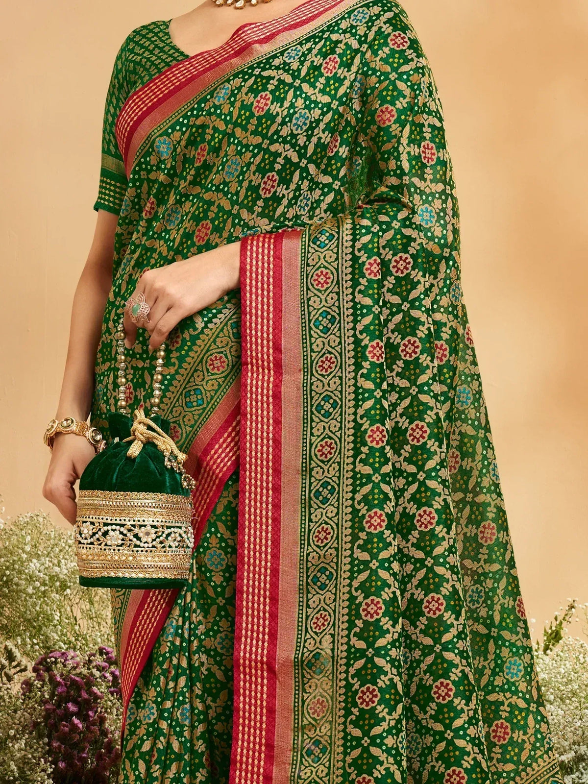 Green floral printed saree with red border, gold embroidery, and matching velvet potli bag for ethnic wear