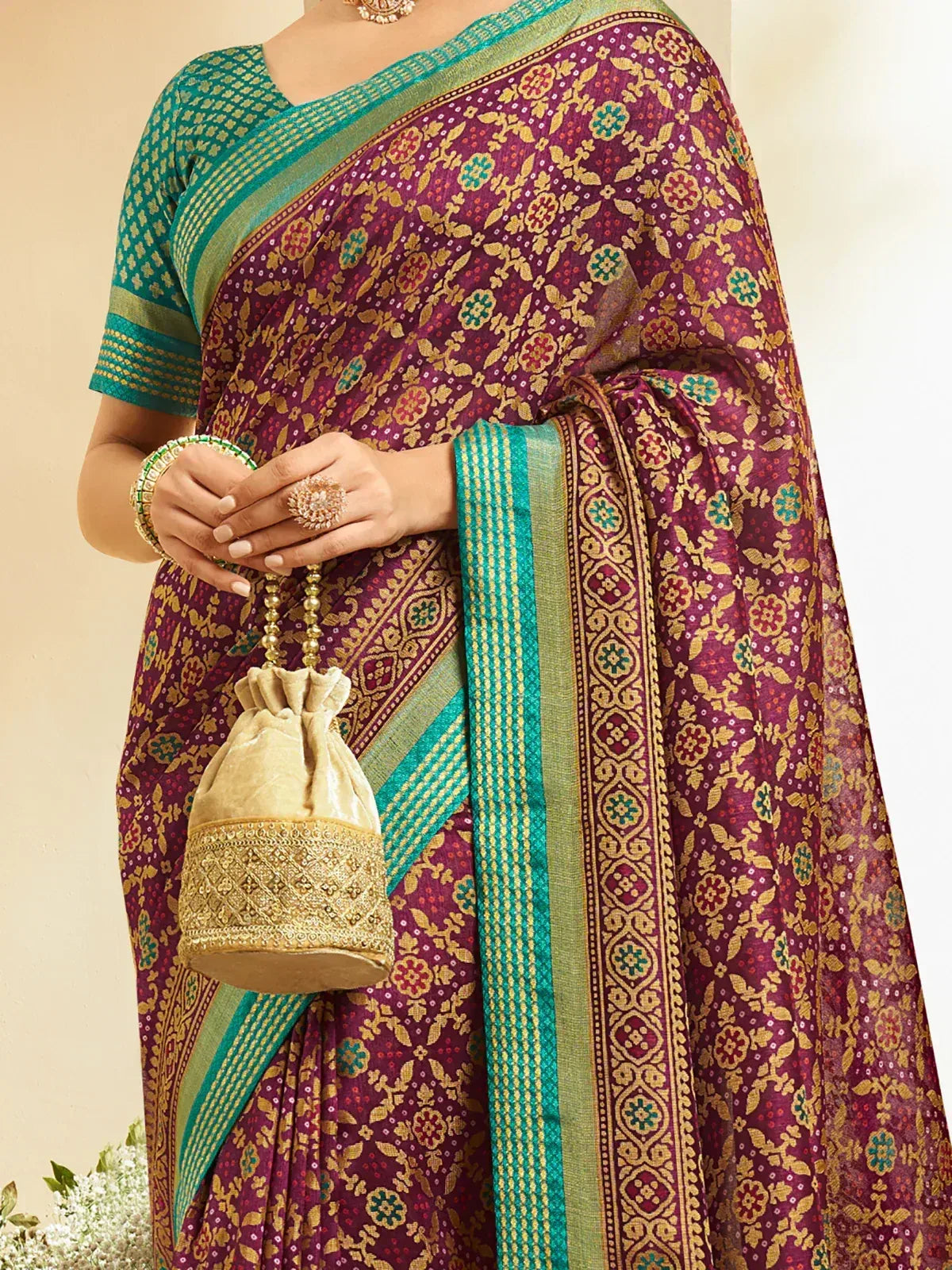 Elegant maroon saree with gold floral patterns and green border, paired with matching blouse and potli bag