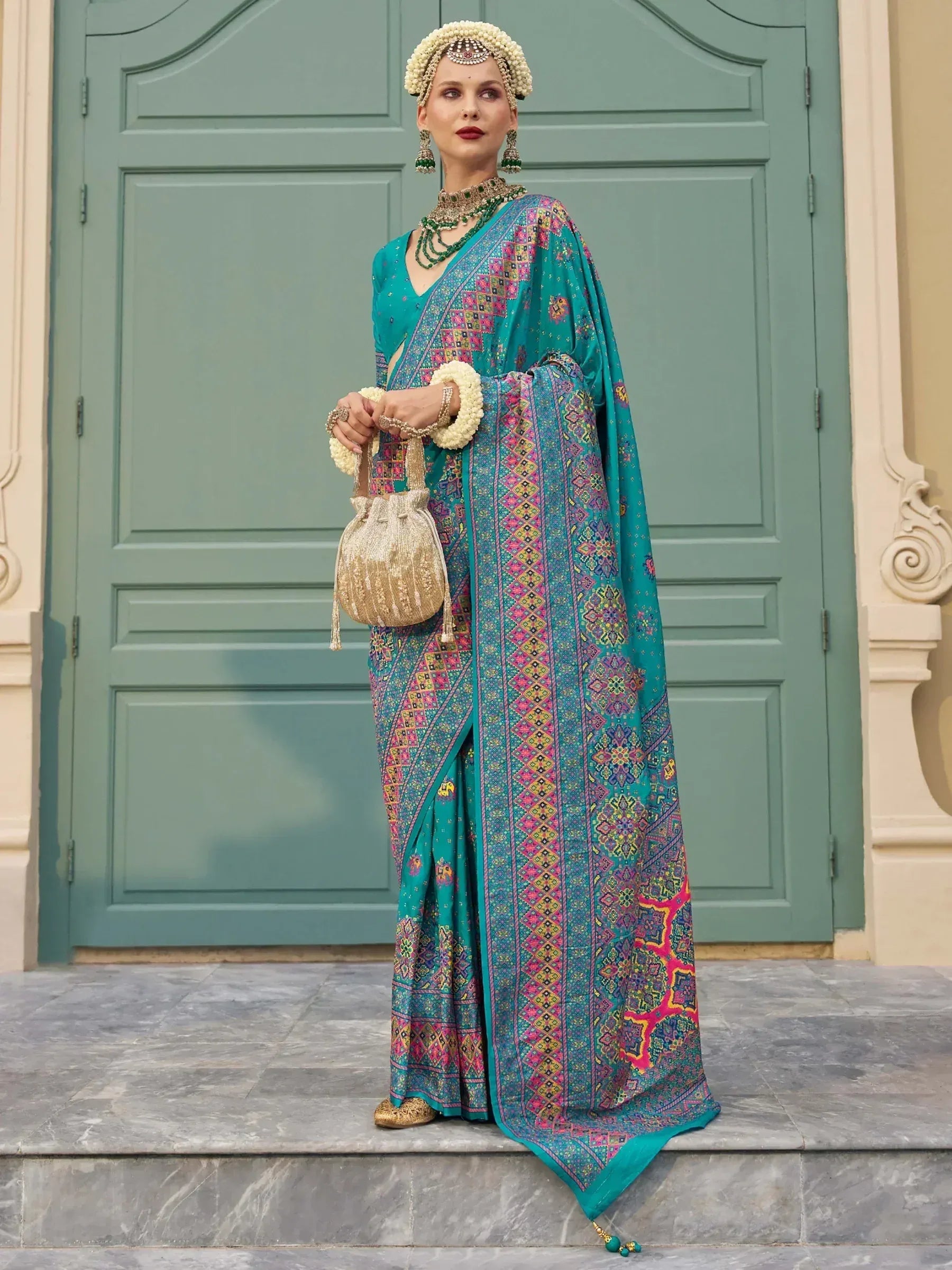 Teal printed saree with pink and gold motifs, paired with traditional jewelry and floral headpiece for ethnic wear
