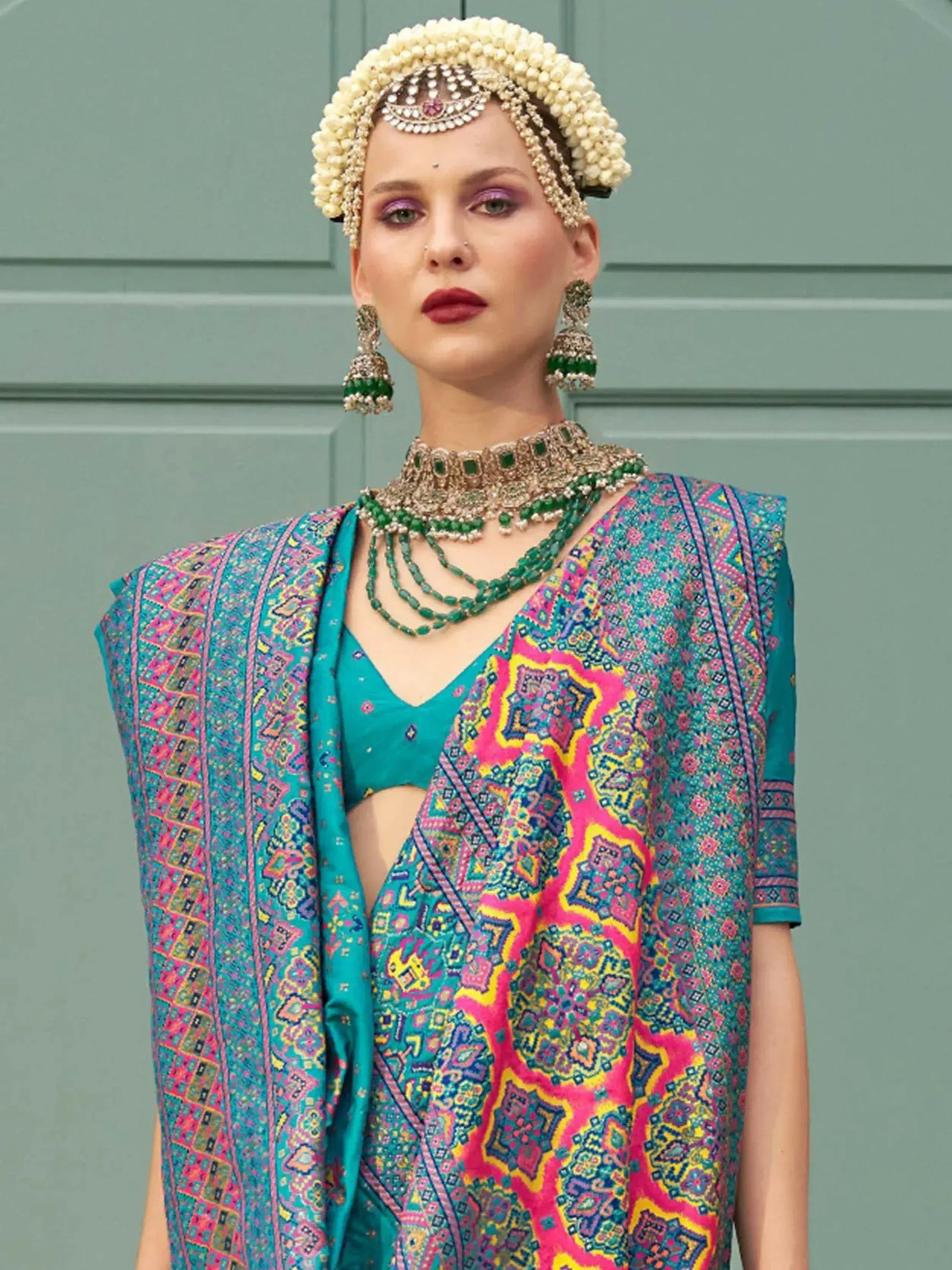 Woman in vibrant Indian ethnic wear with floral headpiece, emerald jewelry, and colorful printed dupatta