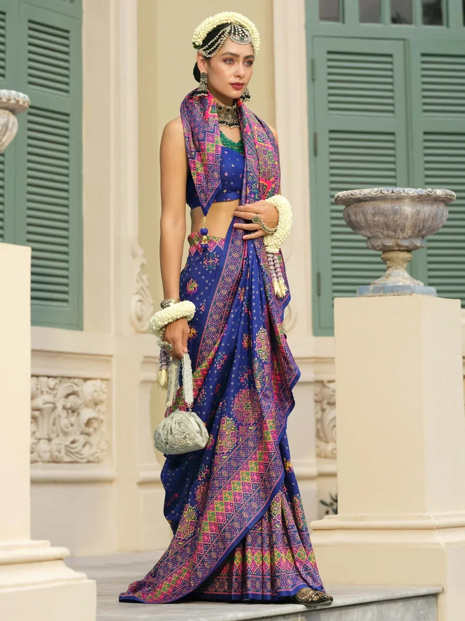 Woman in vibrant blue and pink printed lehenga choli with floral jewelry, perfect for Indian ethnic wear occasions.