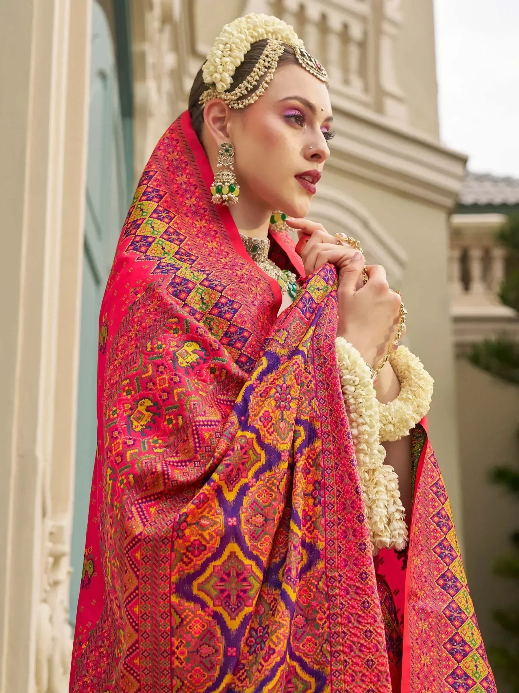 Vibrant pink ethnic saree with intricate geometric patterns, paired with traditional jewelry and floral adornments.