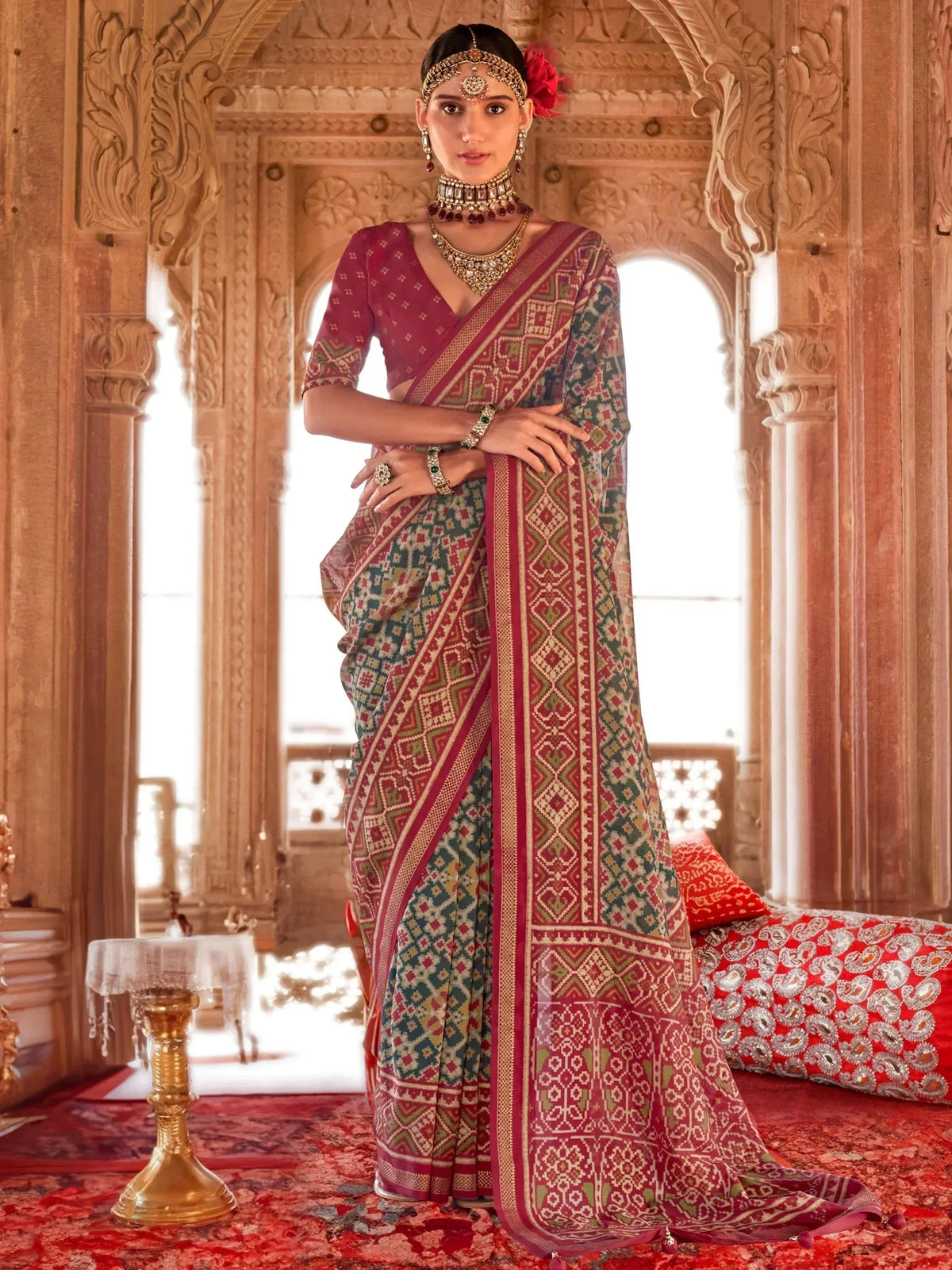 Woman in traditional Indian saree with geometric print, ethnic jewelry, standing in ornate palace setting