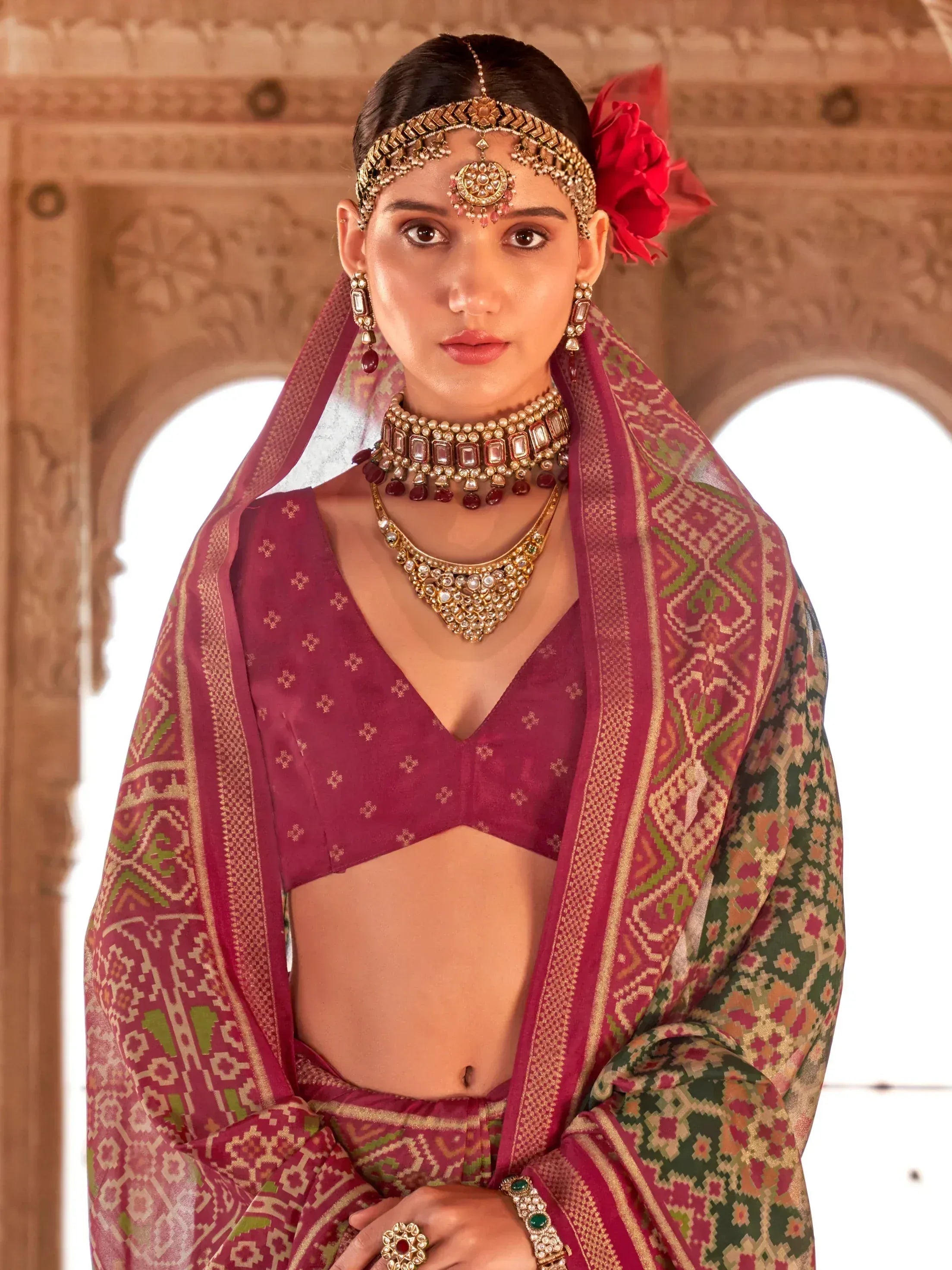 Woman in maroon ethnic lehenga choli with intricate jewelry and patterned dupatta, traditional Indian wear