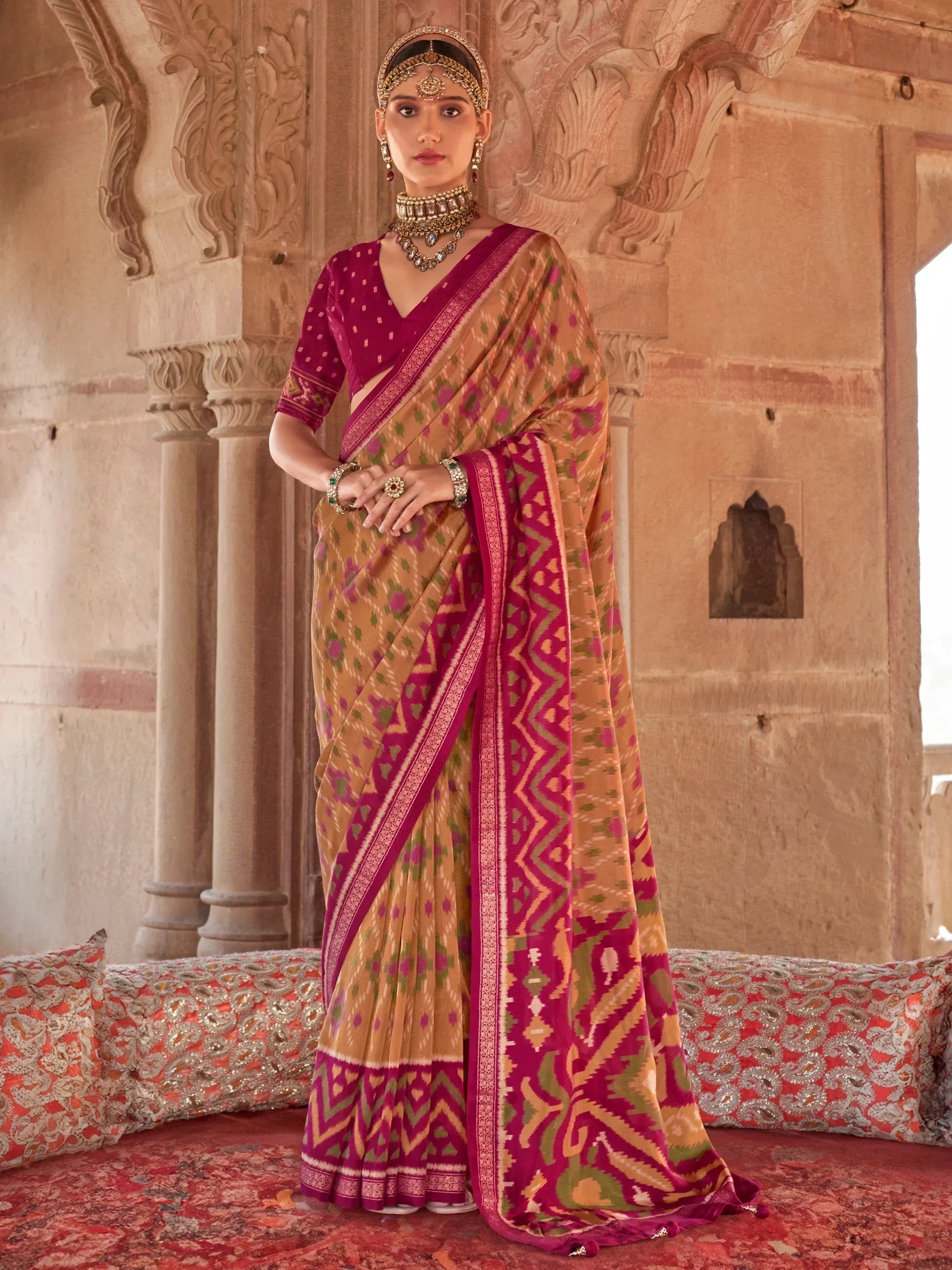 Woman in traditional Indian saree with pink and gold ikat print, paired with ethnic jewelry, standing in palace setting