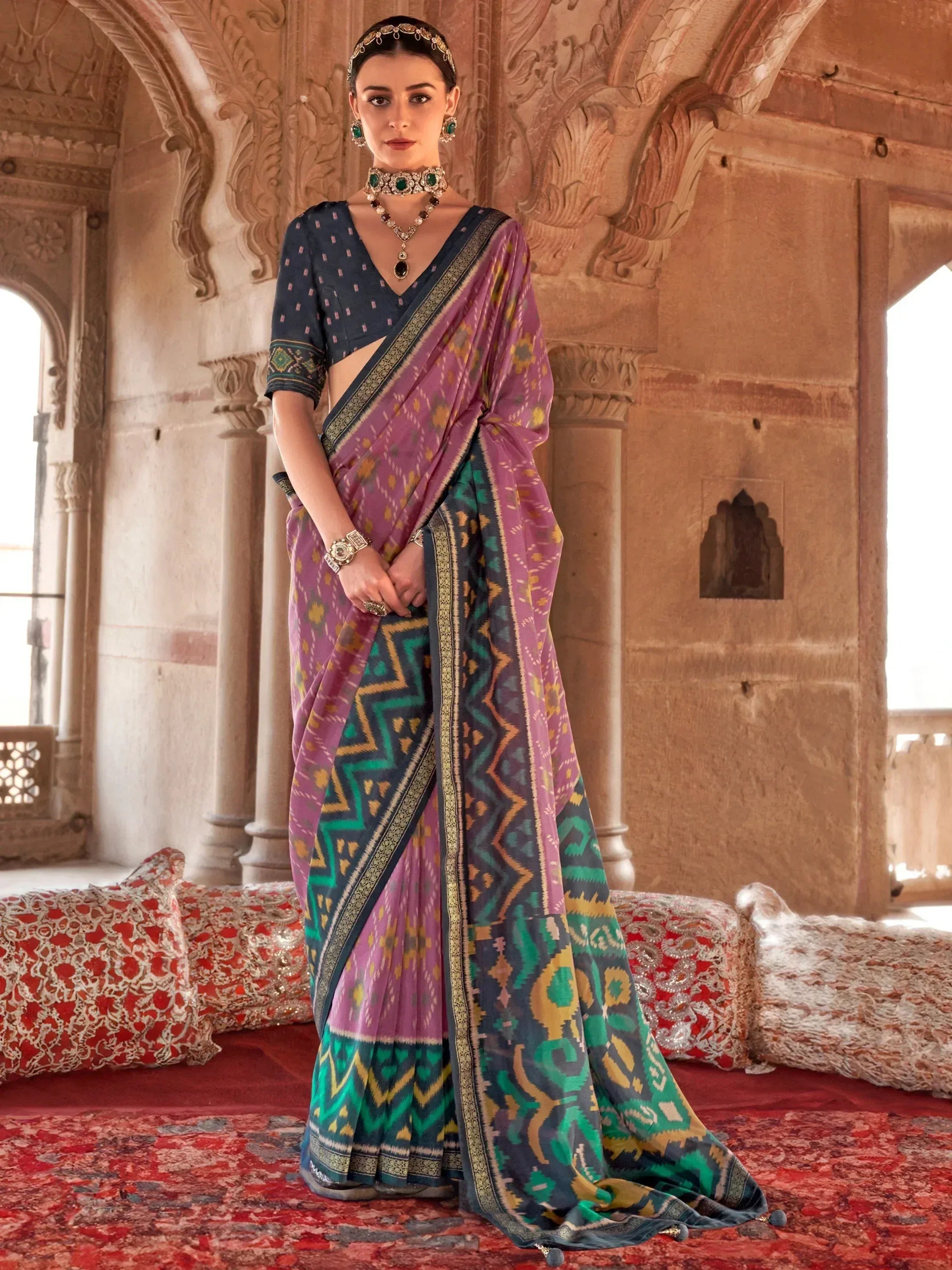 Purple and green ikat saree with gold border, paired with navy blouse, worn in palace setting