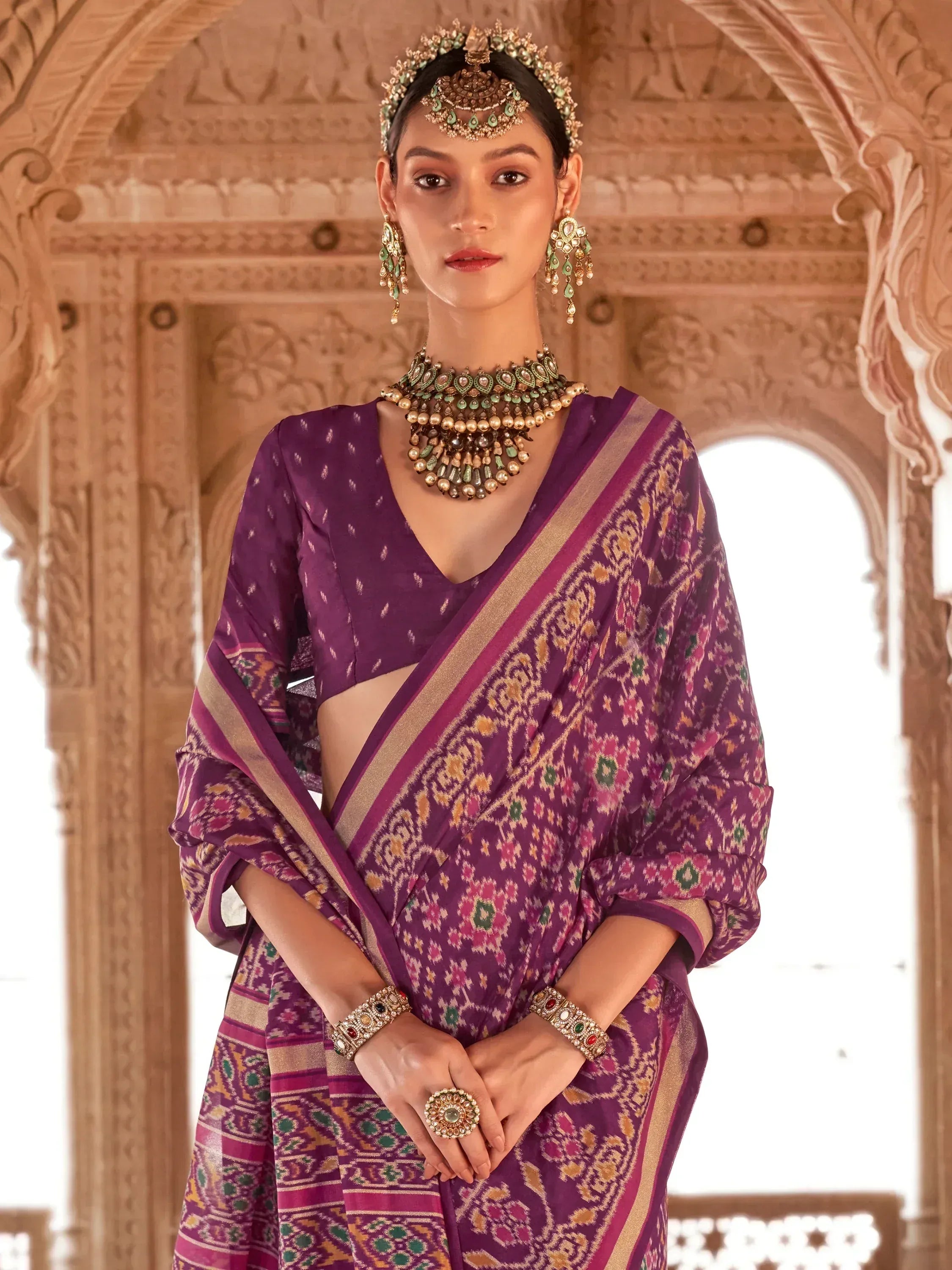 Purple ethnic saree with intricate ikat print, gold border, and traditional jewelry for Indian occasions