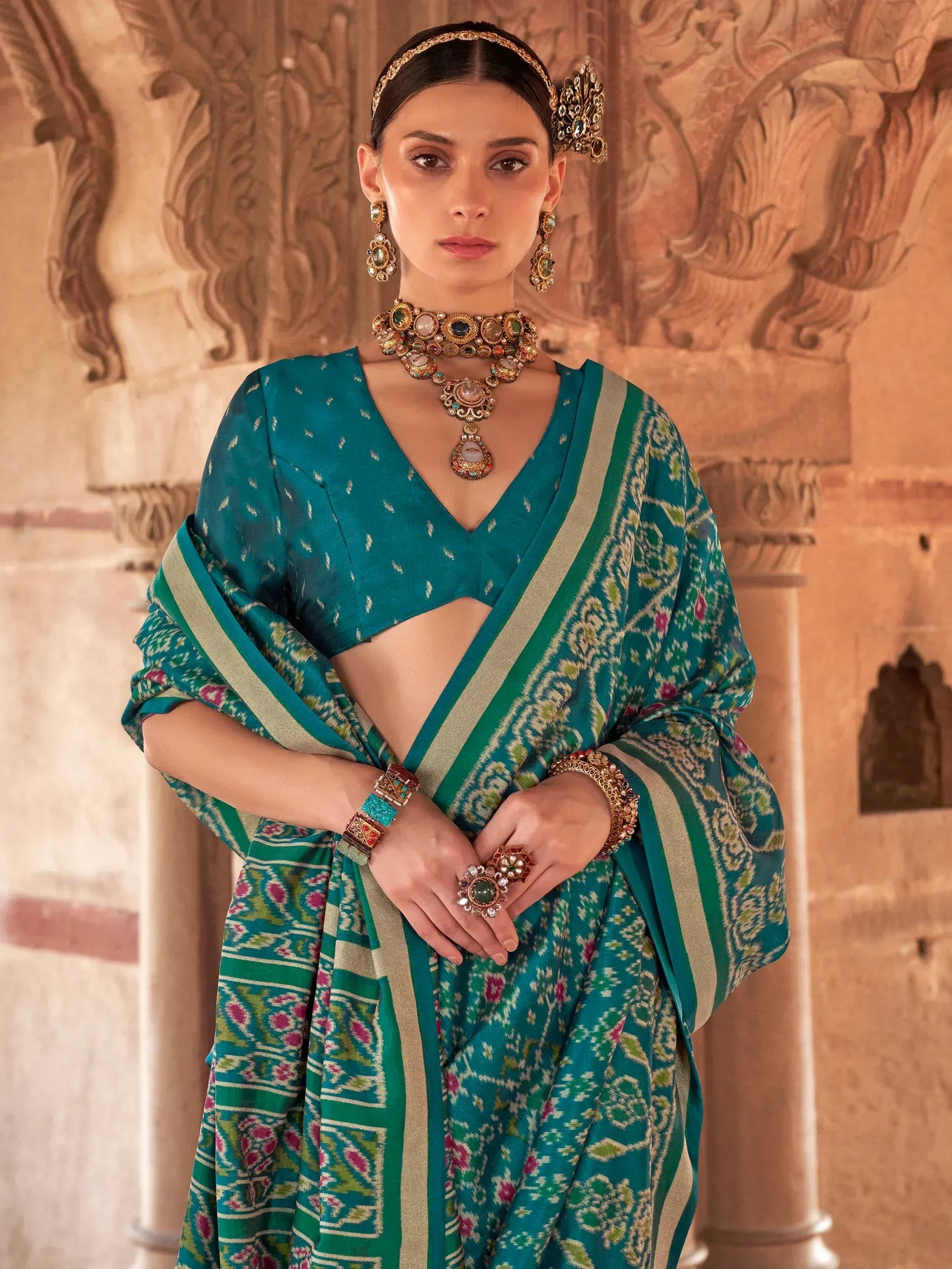 Teal ethnic saree with intricate patterns, paired with traditional jewelry and a V-neck blouse.