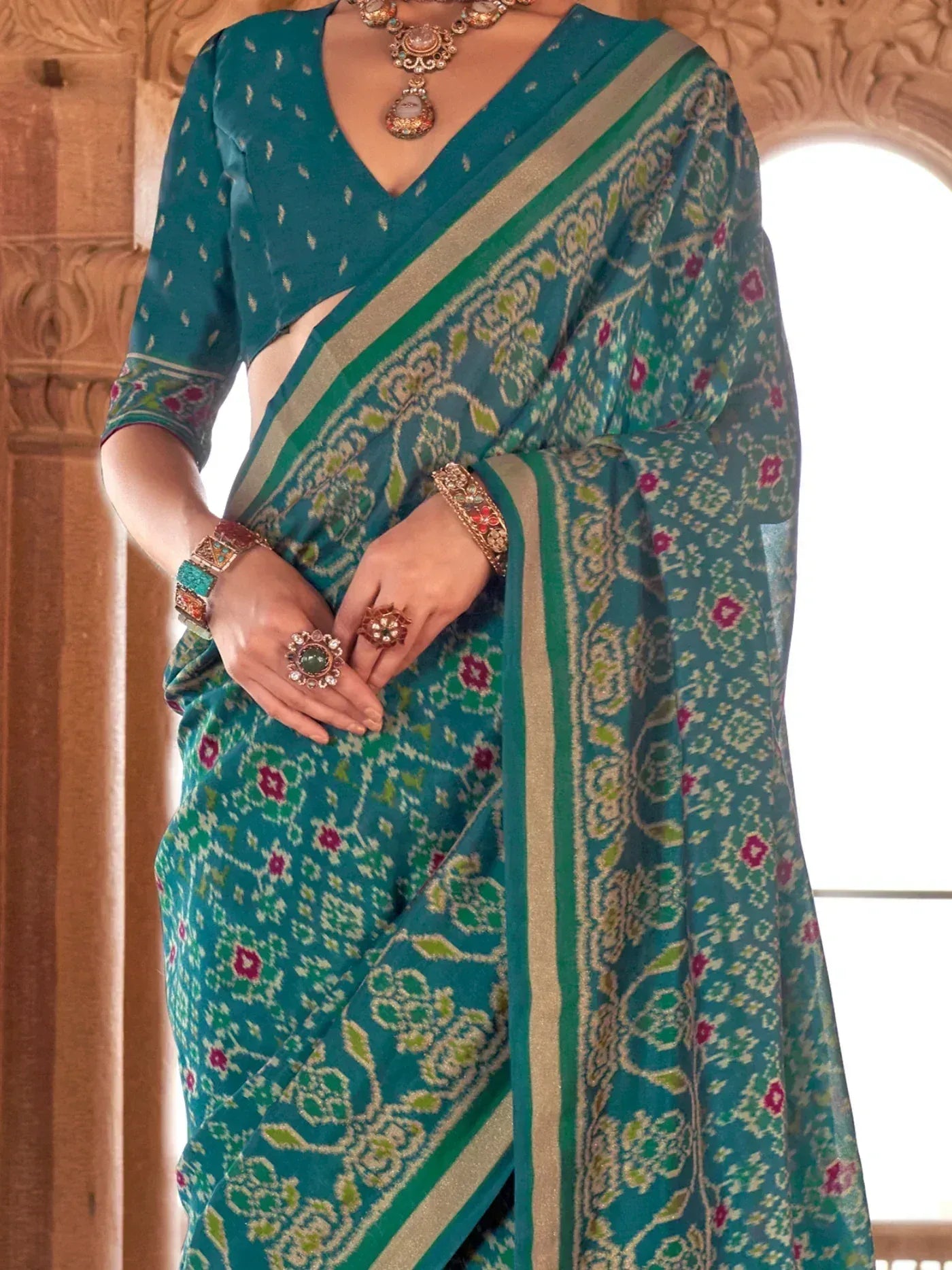 Teal floral print saree with gold border, paired with matching blouse and traditional jewelry, perfect for ethnic occasions.