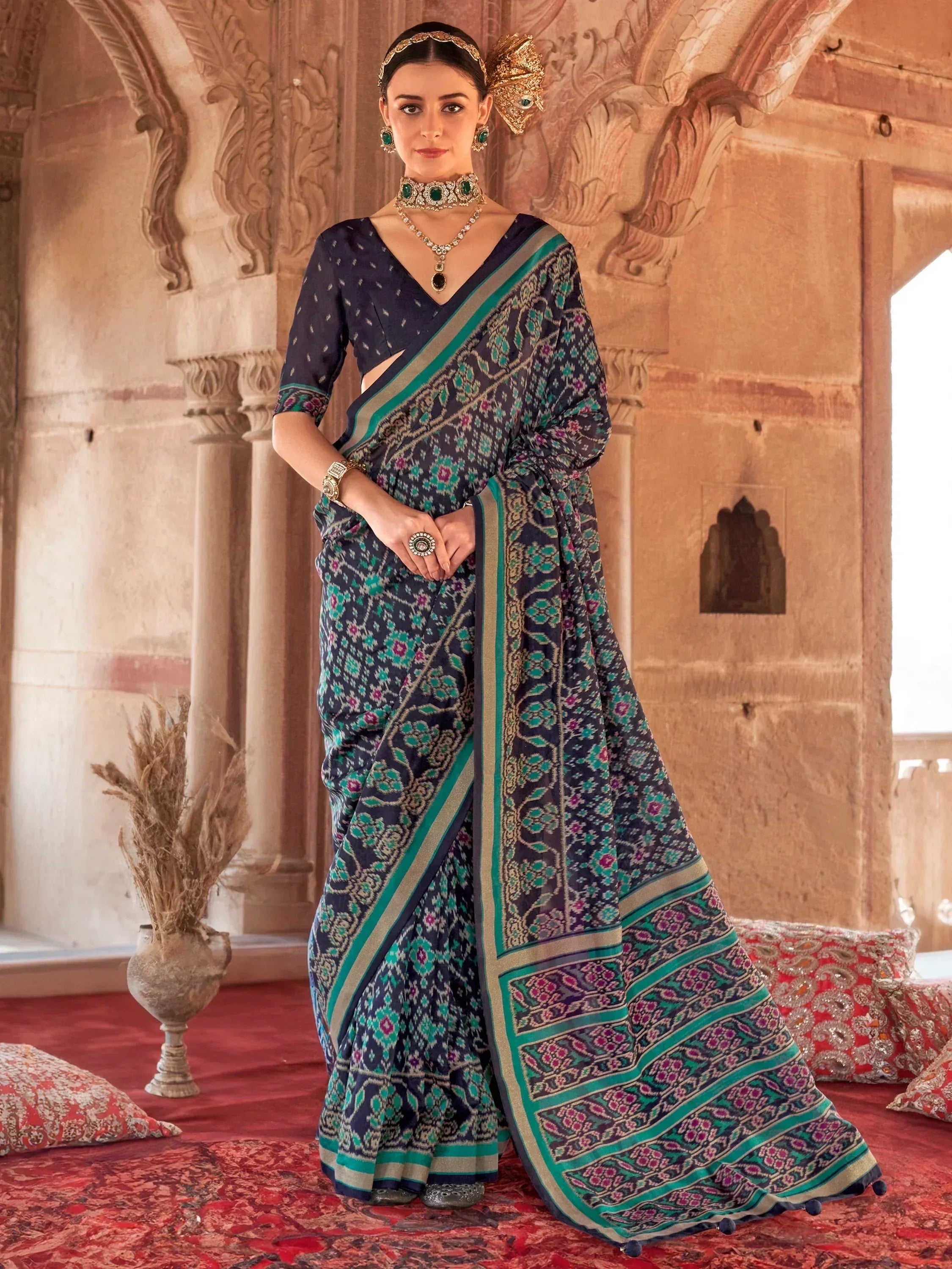Elegant navy blue saree with teal and gold ikat print, paired with designer jewelry, perfect for ethnic occasions.