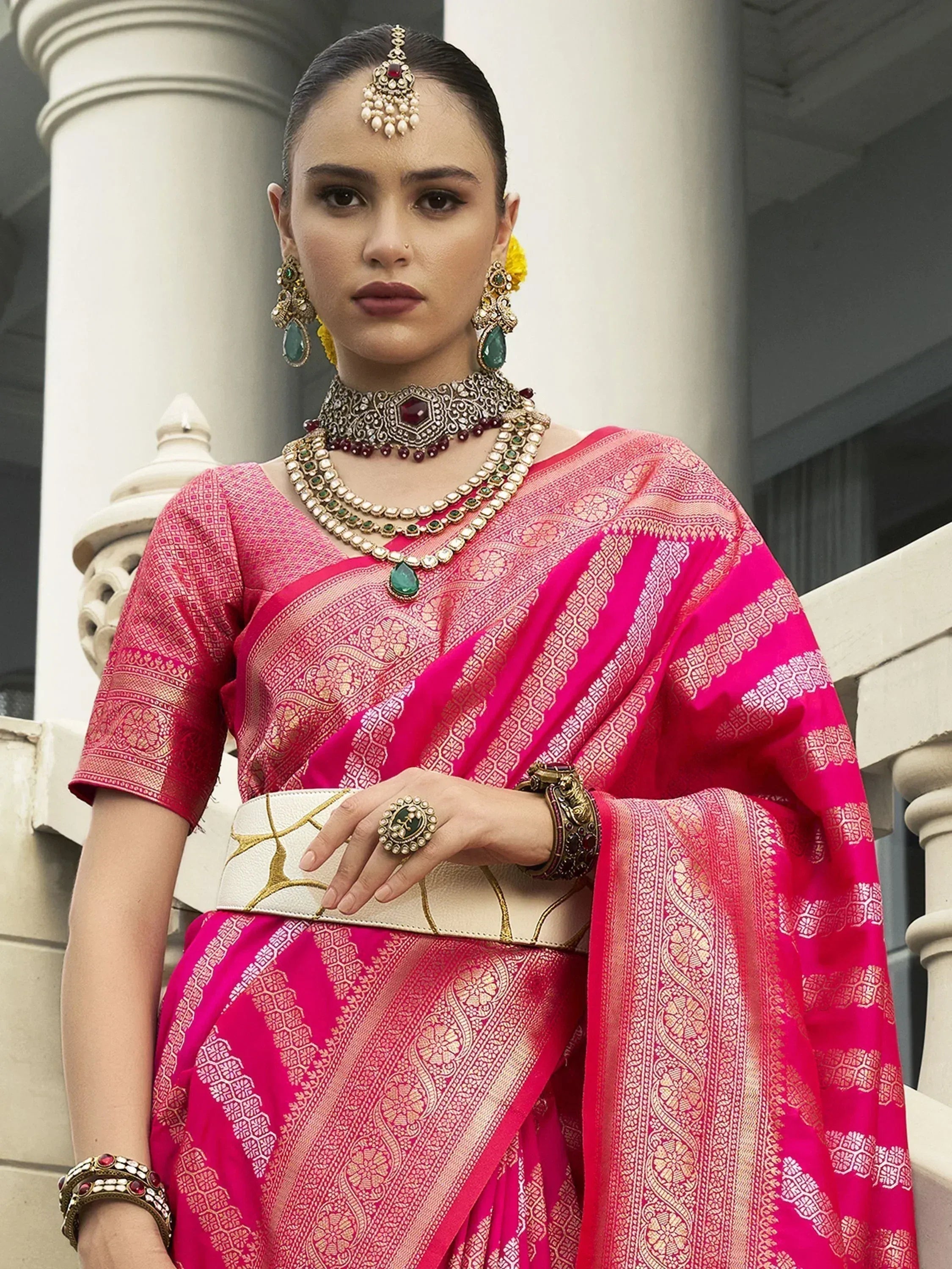 Woman in vibrant pink designer saree with gold embroidery, traditional Indian jewelry, and floral hair accessory