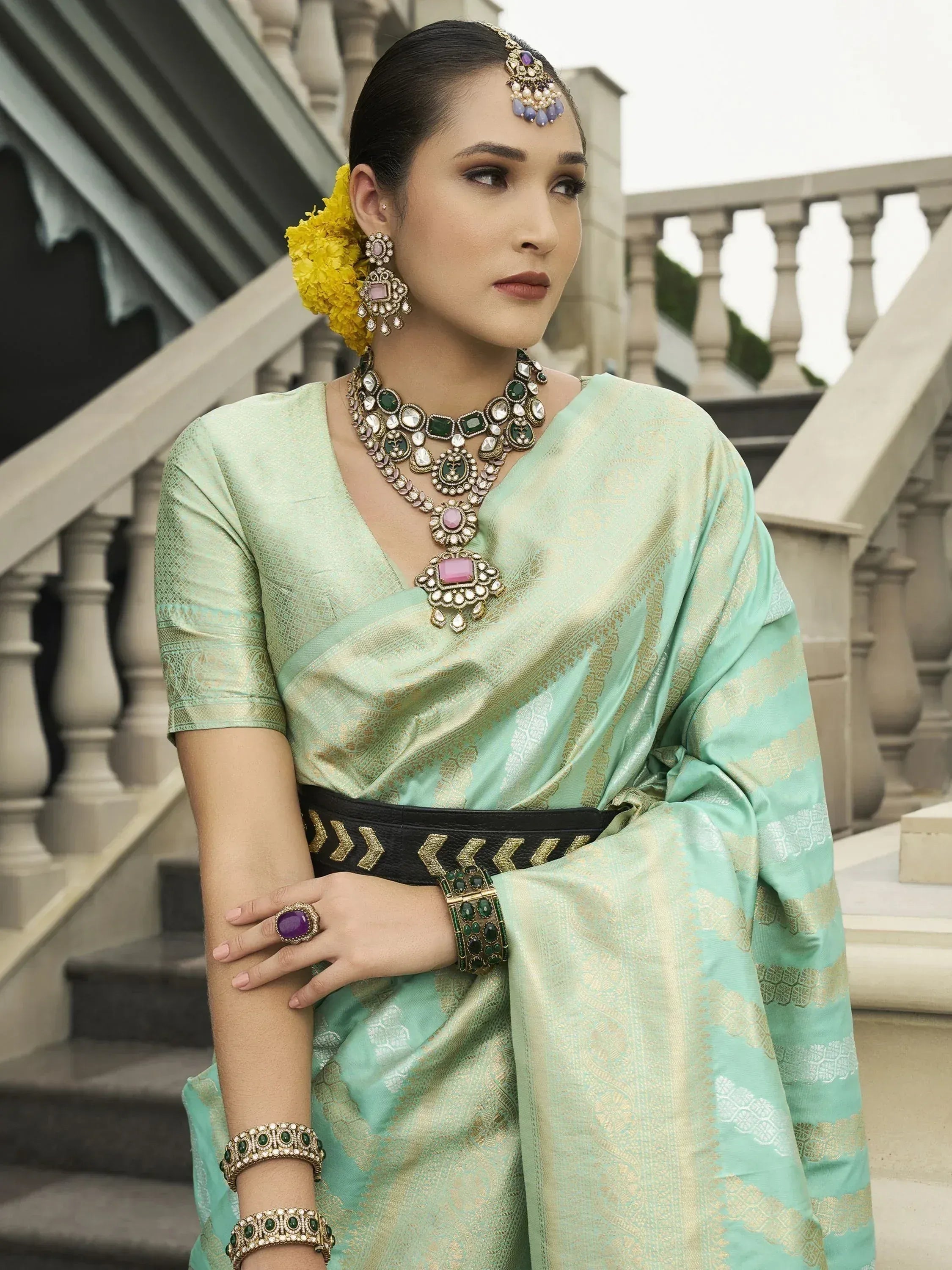 Mint green designer saree with gold embroidery, paired with statement jewelry and yellow floral hair accessory.