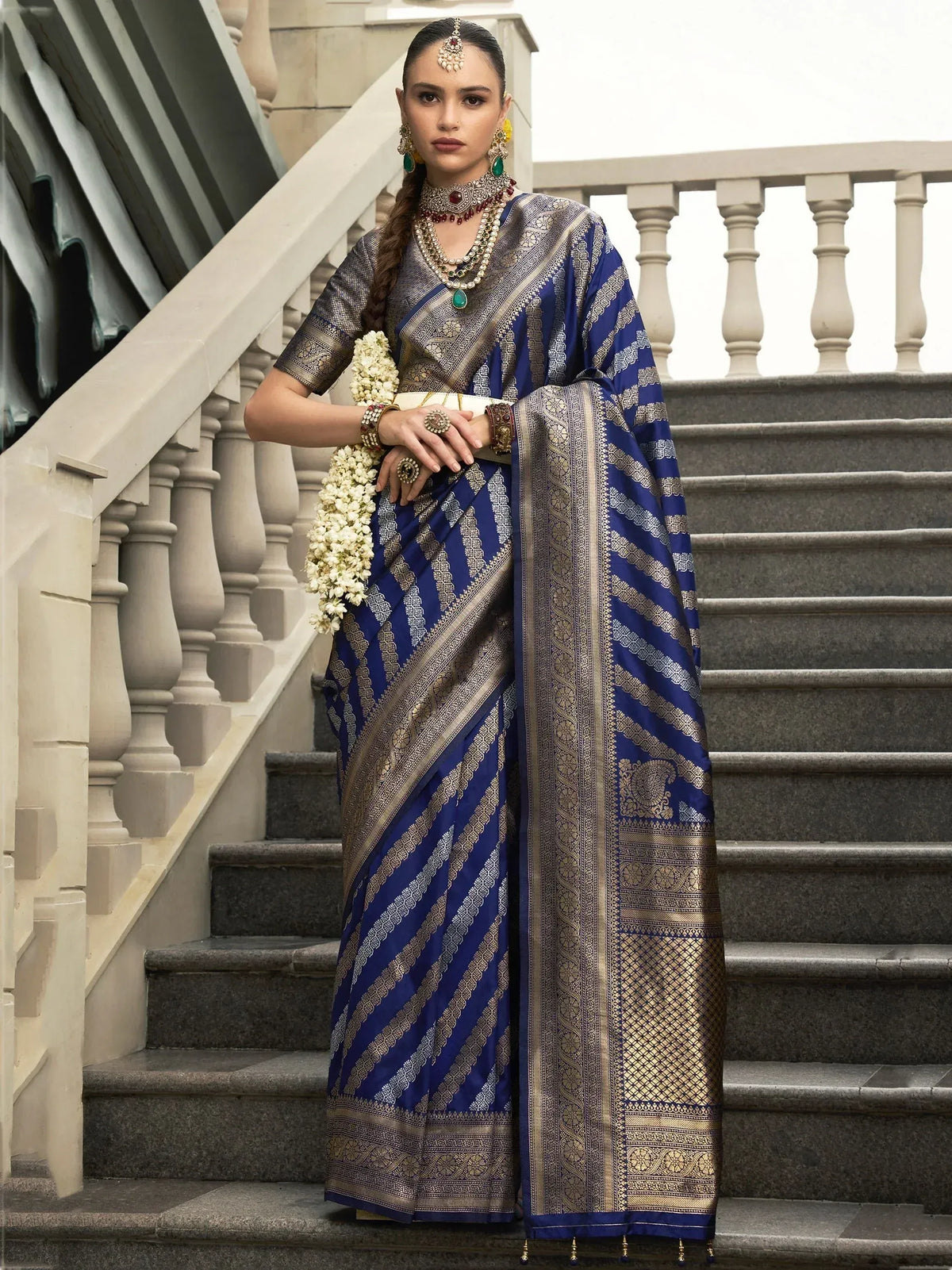 Blue and gold designer saree with intricate patterns, worn with traditional jewelry on stone stairs