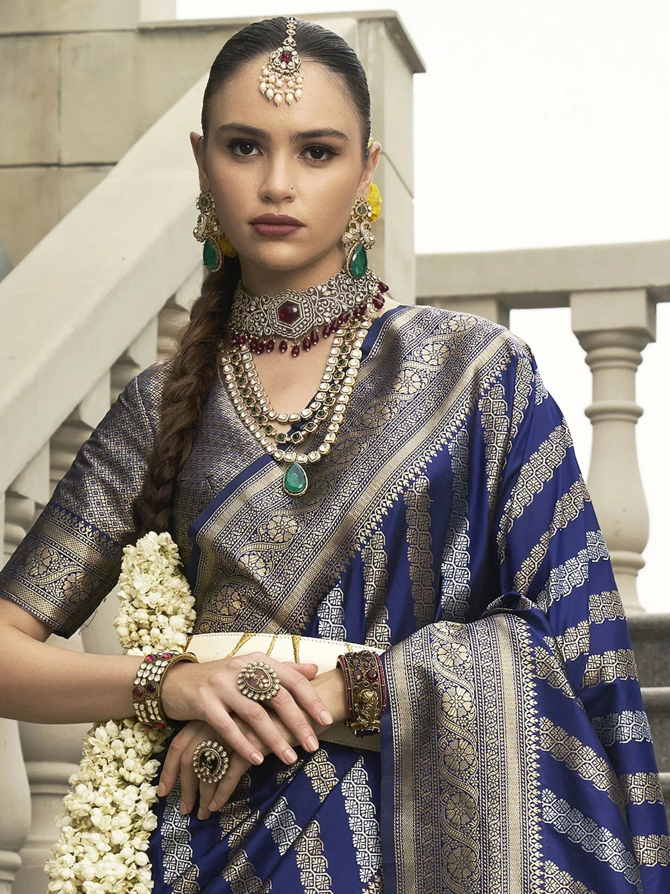 Elegant woman in royal blue ethnic saree with gold embroidery, traditional jewelry, and floral garland