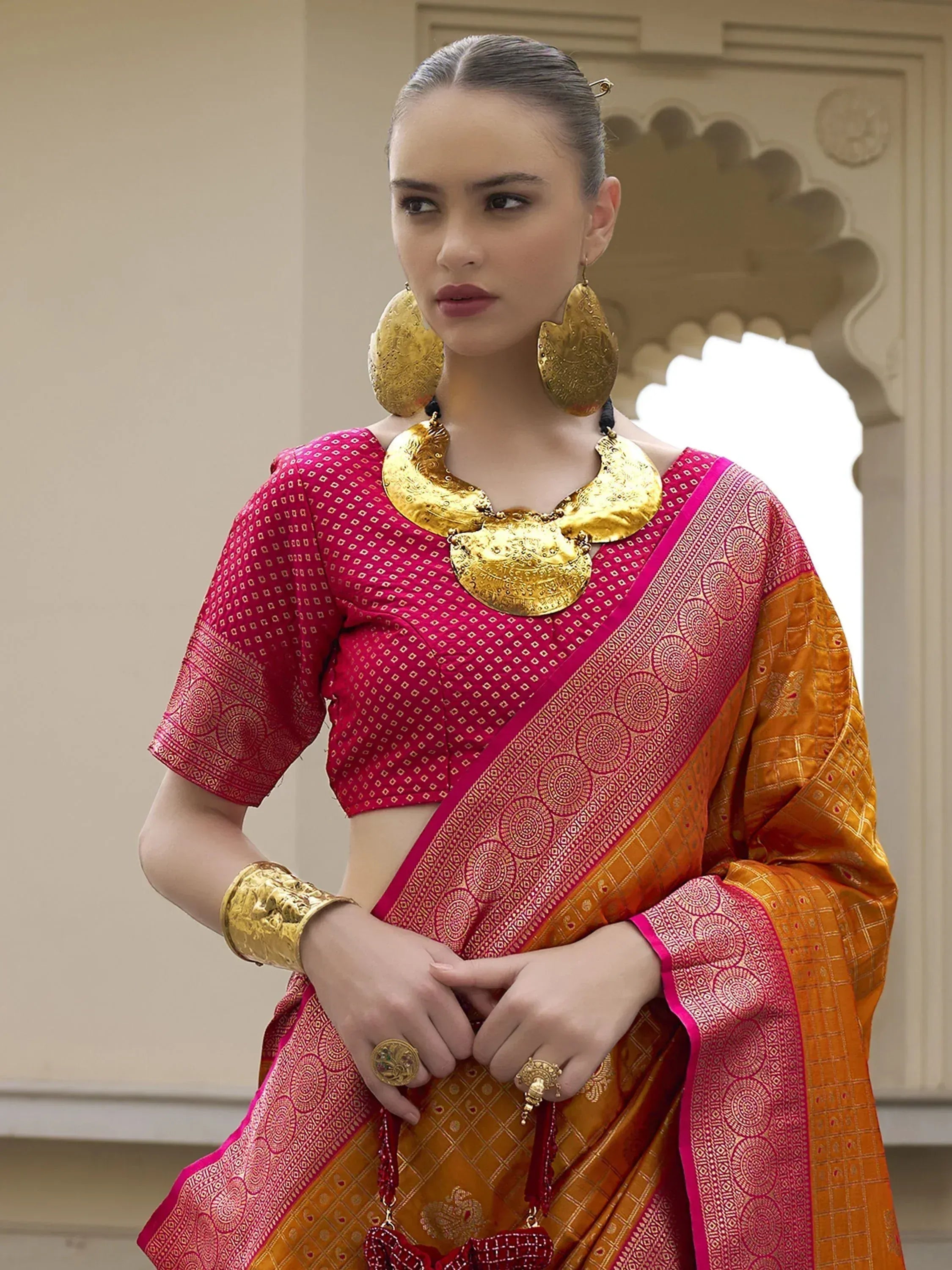 Woman in vibrant pink and orange ethnic saree with gold jewelry, traditional Indian attire