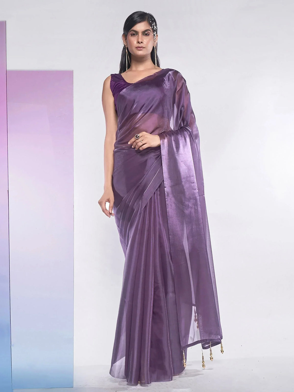 Purple satin saree with sheer pallu and gold tassels, styled with ethnic jewelry for Indian occasions