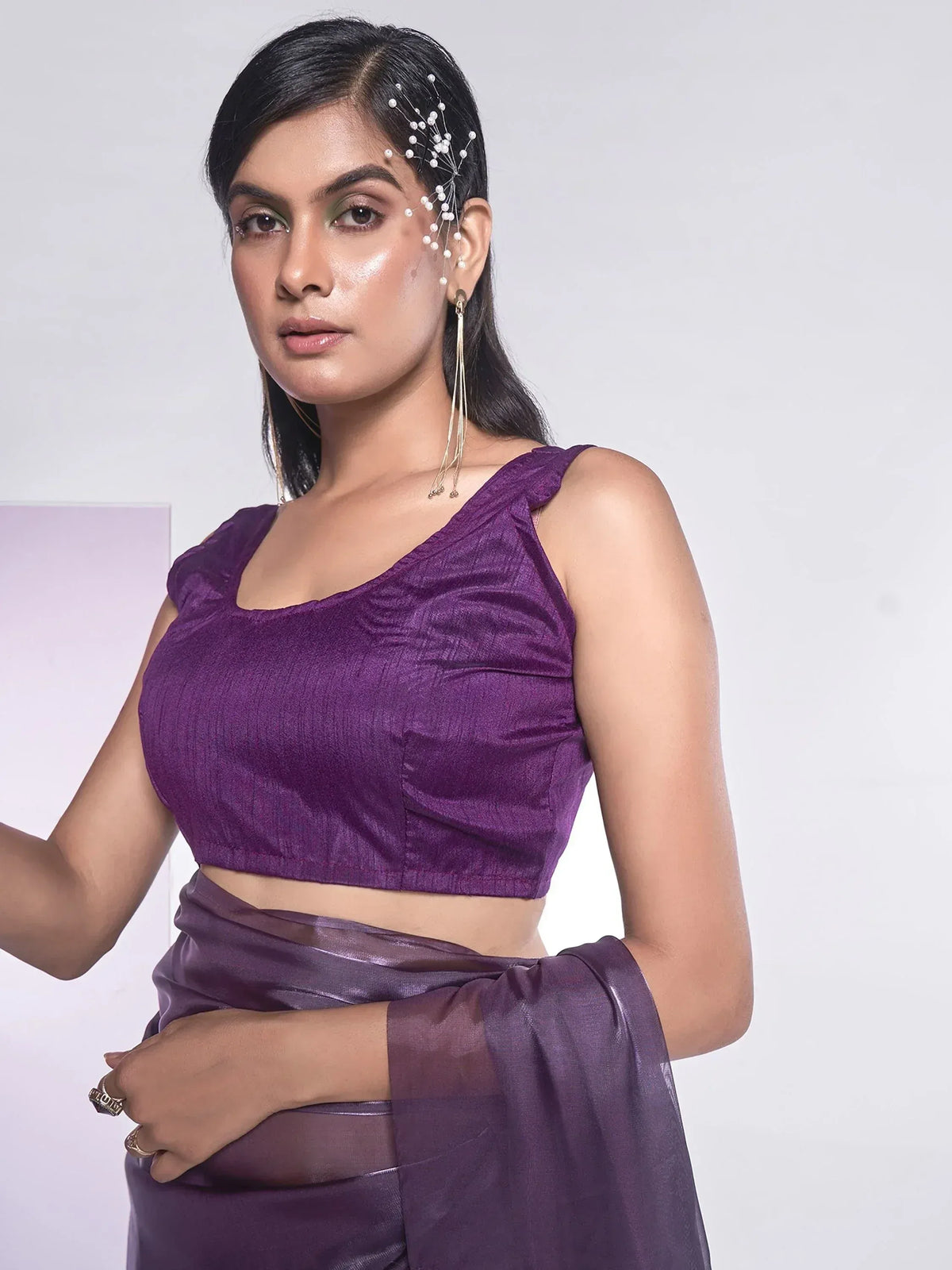 Purple ethnic saree with ruffled blouse, pearl hair accessory, and gold earrings for festive occasions