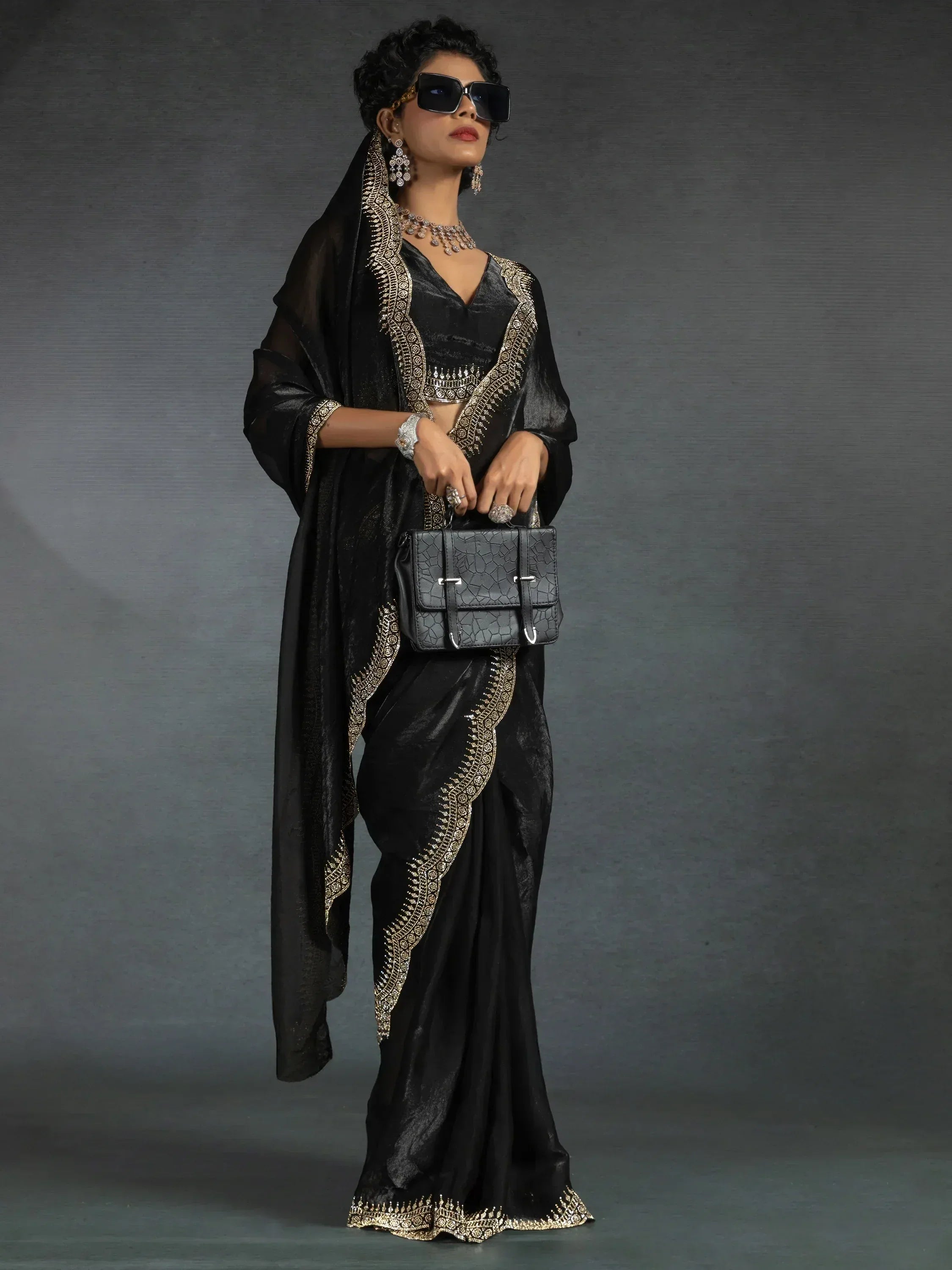 Black velvet saree with gold embroidery, paired with statement jewelry and sunglasses for a chic ethnic look.