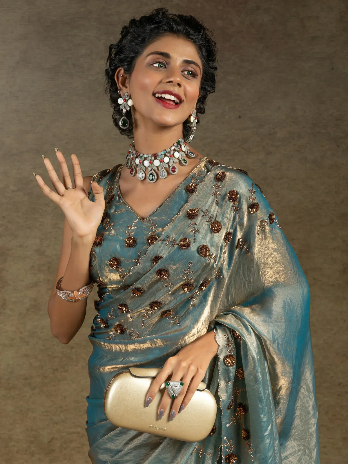 Elegant woman in blue embroidered saree with statement jewelry and gold clutch