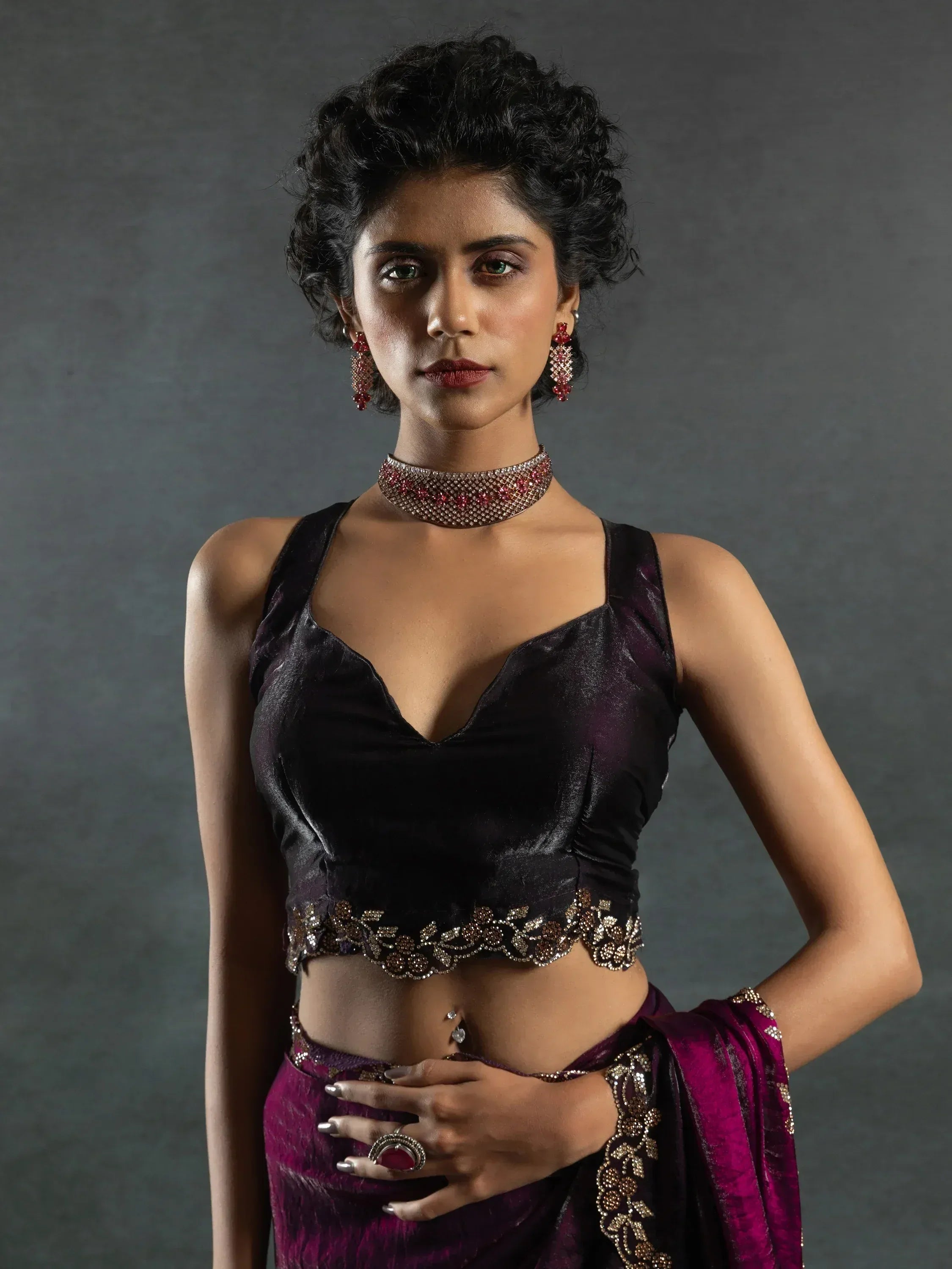 Elegant woman in purple velvet lehenga choli with intricate gold embroidery and red jewelry