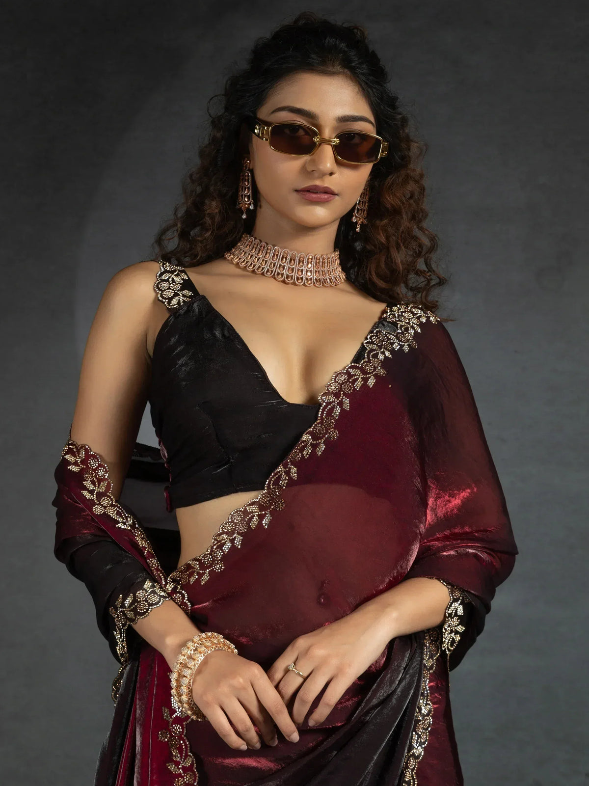 Elegant maroon and black saree with gold embroidery, paired with statement jewelry and sunglasses
