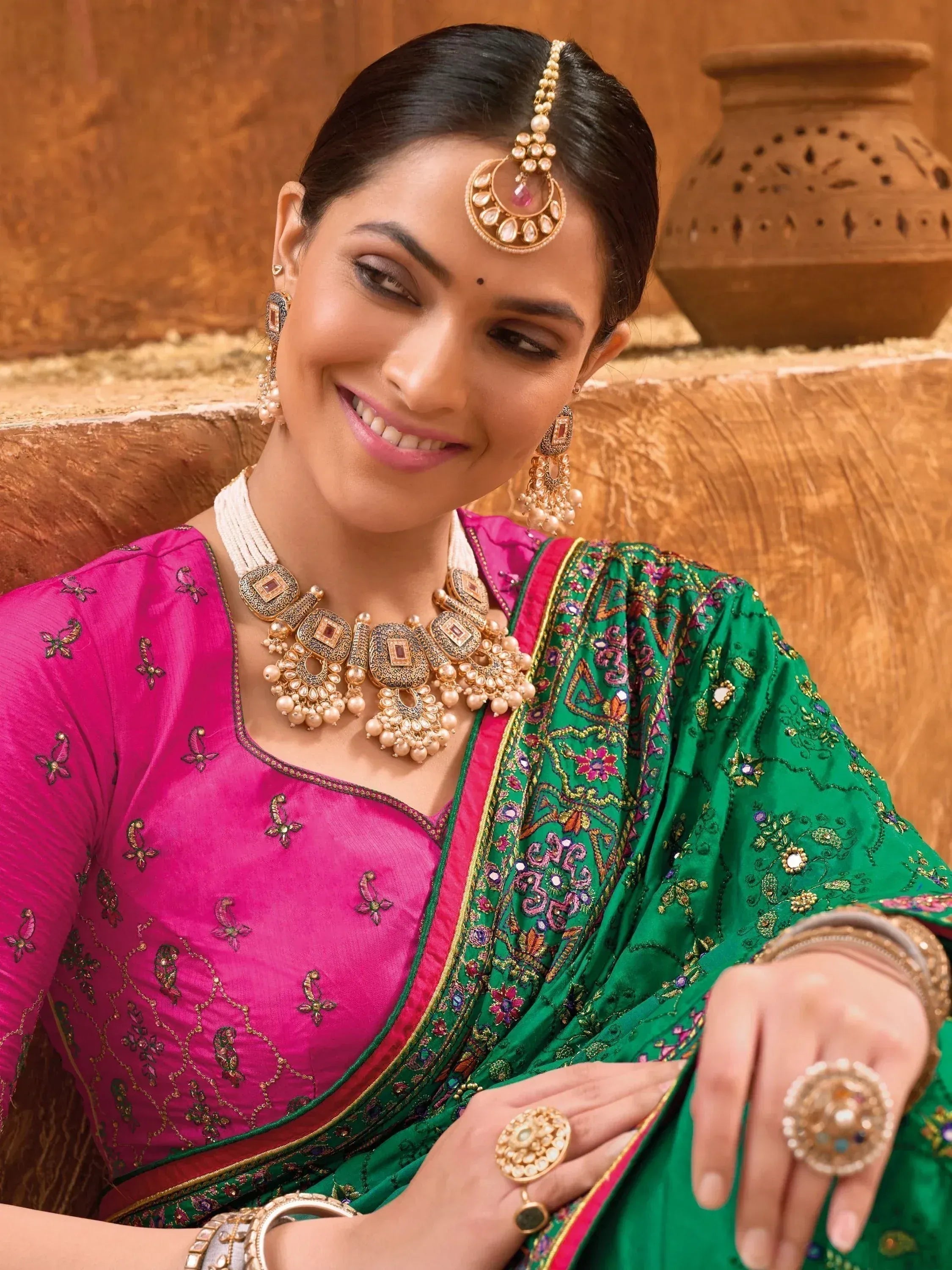 Woman in pink and green embroidered Indian saree with gold jewelry, traditional ethnic wear
