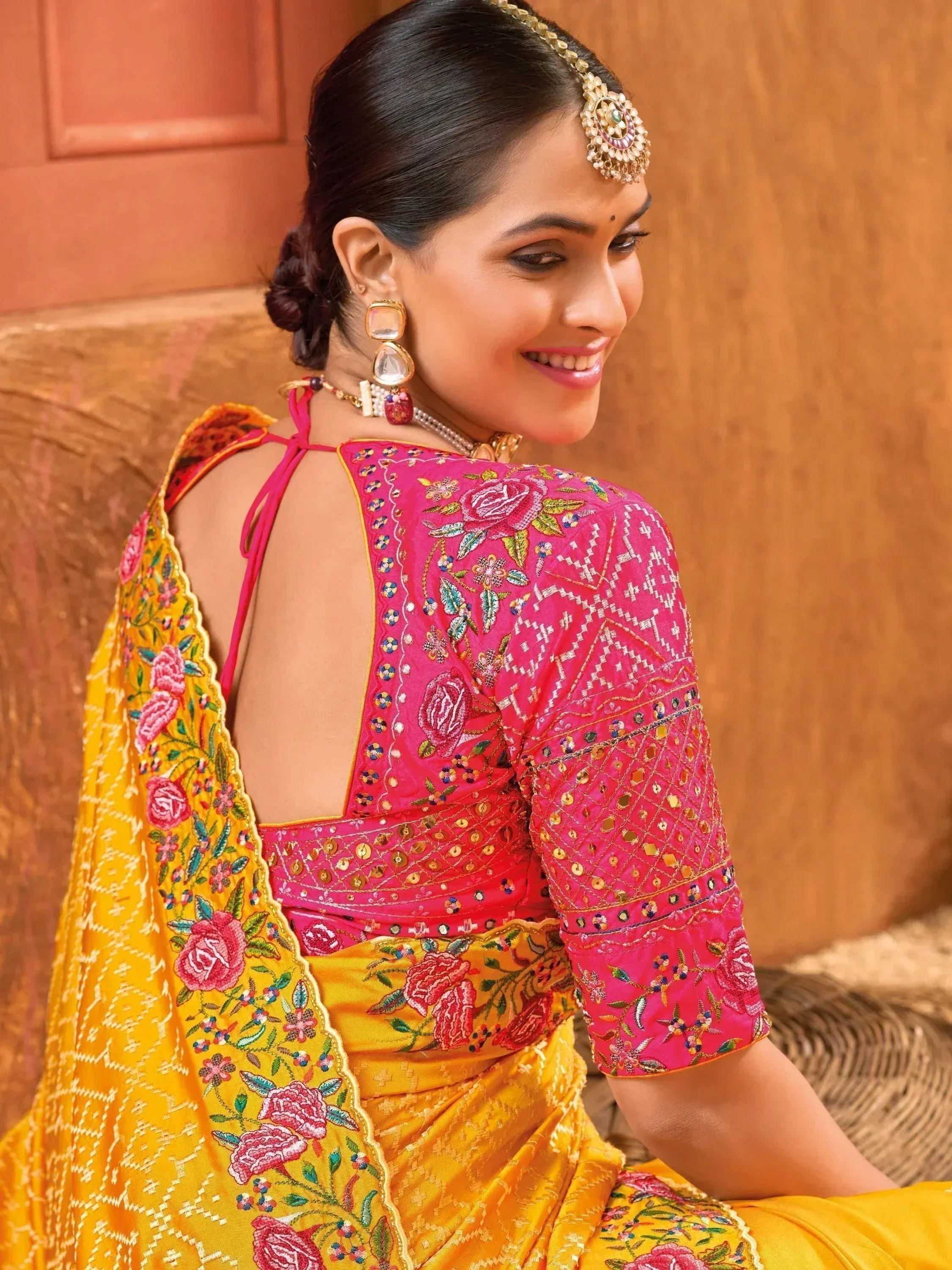 Woman in vibrant pink and yellow embroidered ethnic saree with floral motifs and backless blouse design