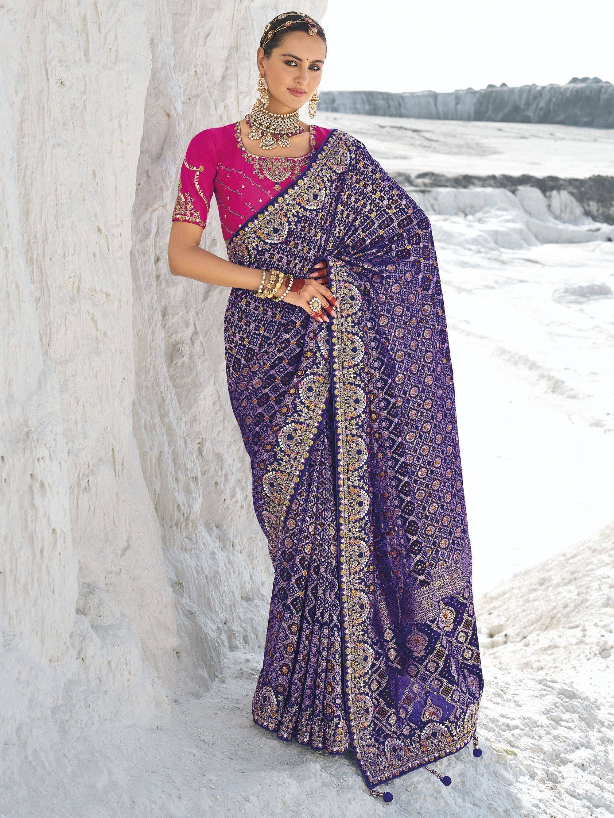 Woman in purple embroidered saree with pink blouse, traditional Indian ethnic wear, standing against white textured wall