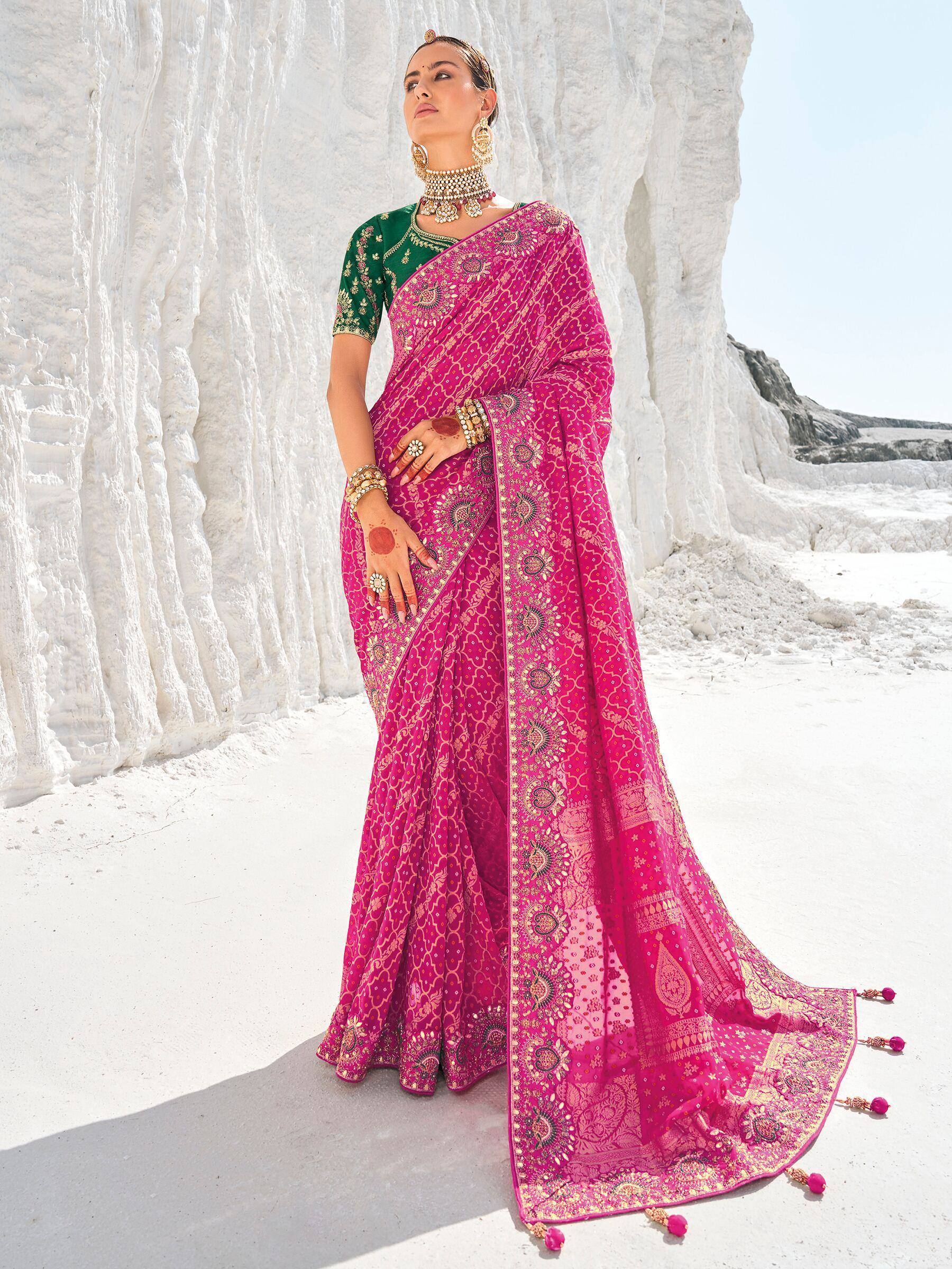 Woman in vibrant pink embroidered saree with green blouse, traditional Indian ethnic wear, standing against white rock formations