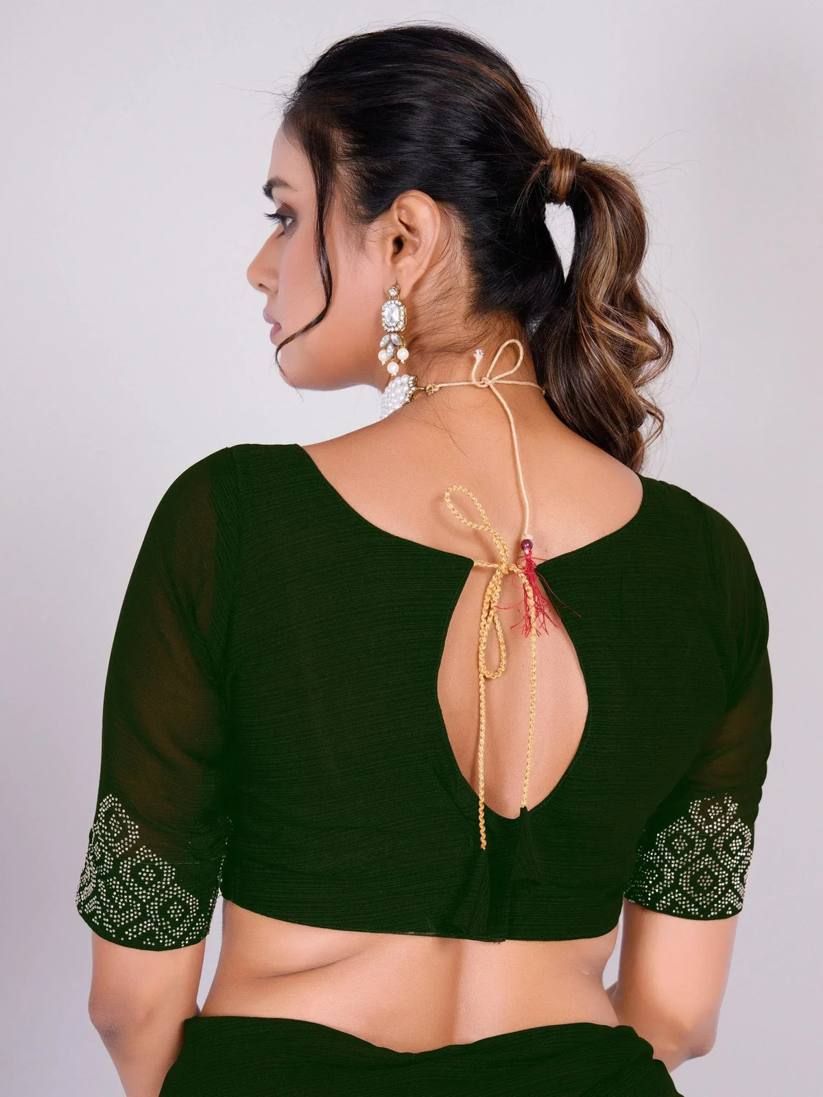 Green ethnic blouse with back cutout, tie-up detail, and embellished sleeves, paired with statement earrings.