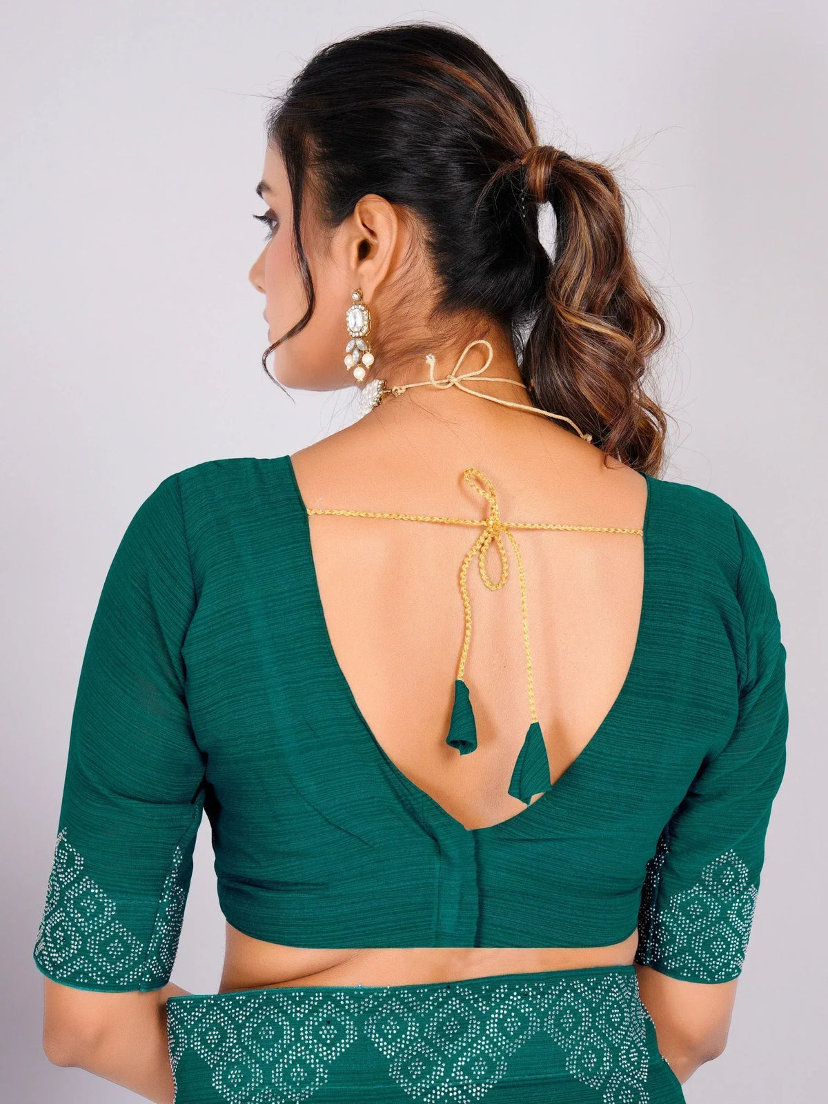 Emerald green saree blouse with open back, gold tie-up, and tassels, paired with statement earrings.