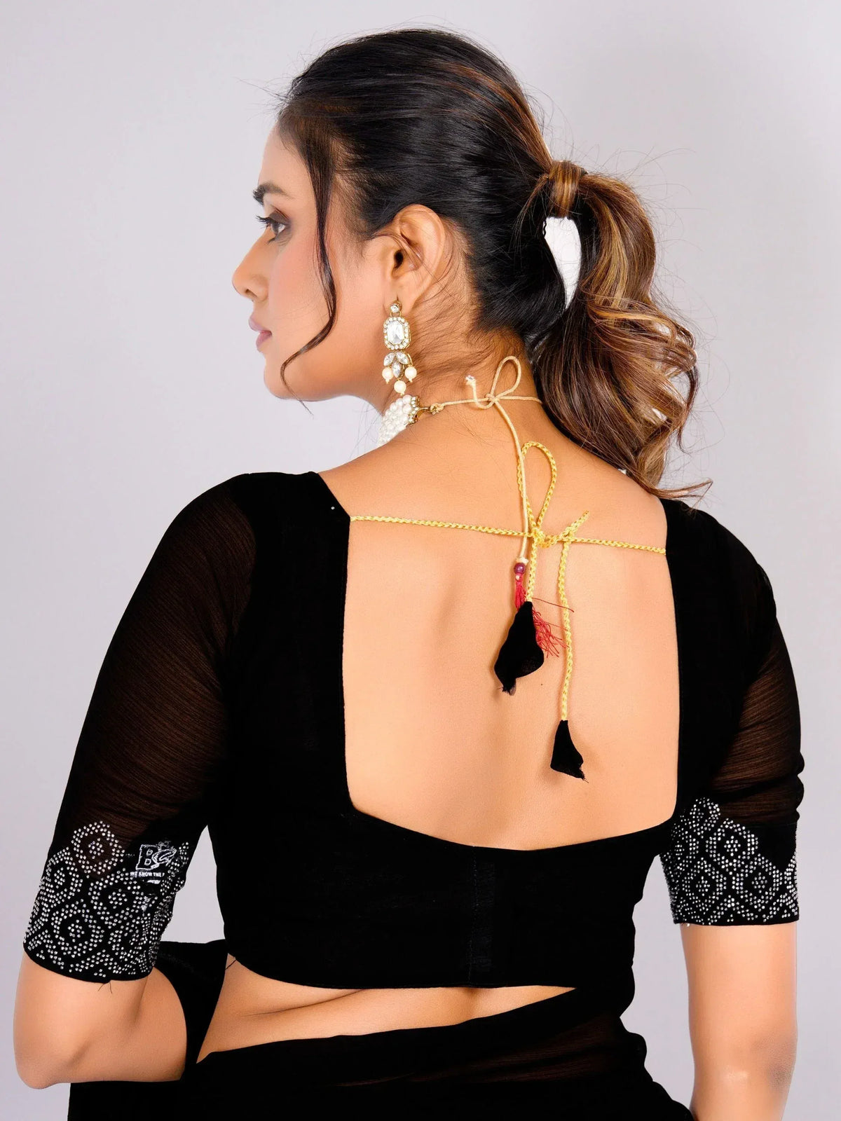 Black velvet blouse with sheer sleeves, back tie detail, and tassels, paired with ethnic jewelry for Indian wear.