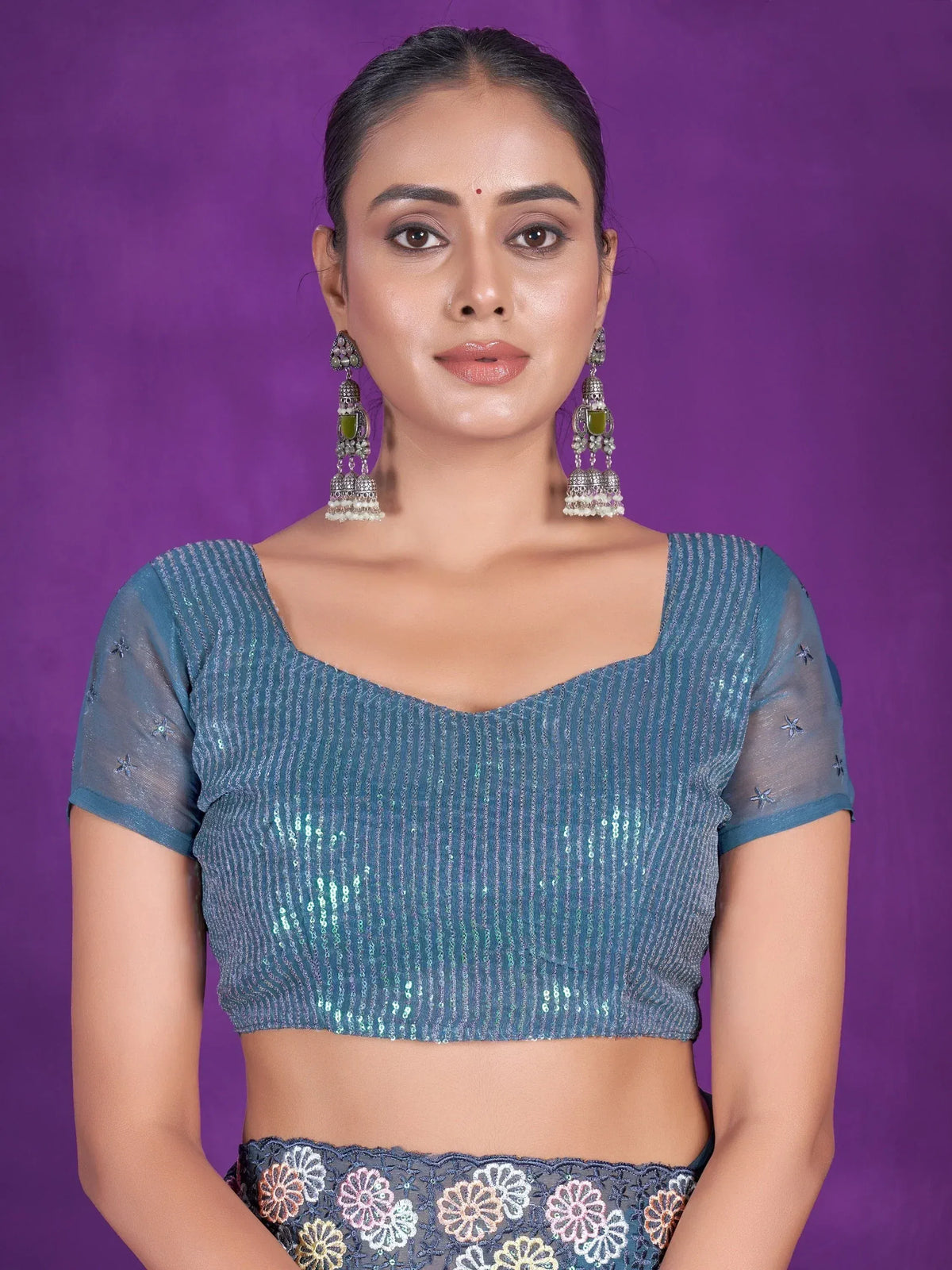Blue sequin lehenga choli top with sheer sleeves and floral embroidery, paired with traditional jhumka earrings.