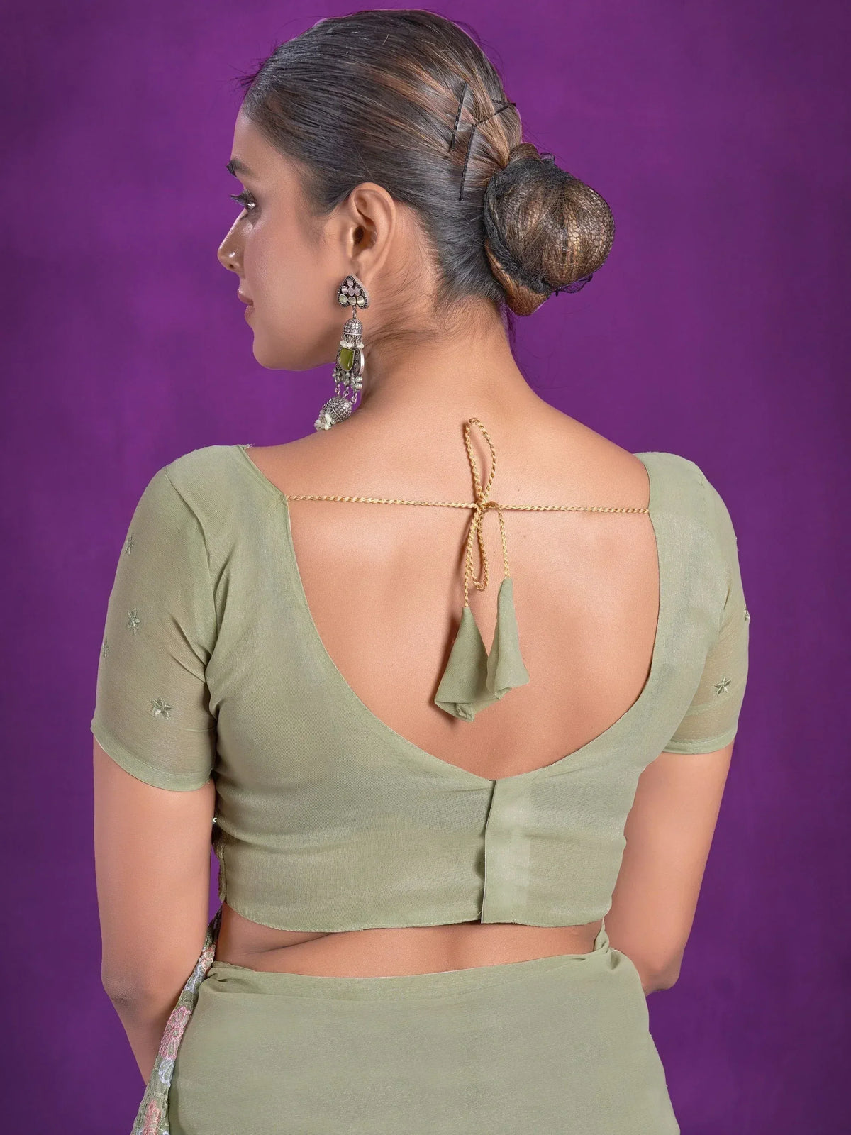 Olive green saree blouse with open back, tie-up detail, and star embroidery, paired with statement earrings.