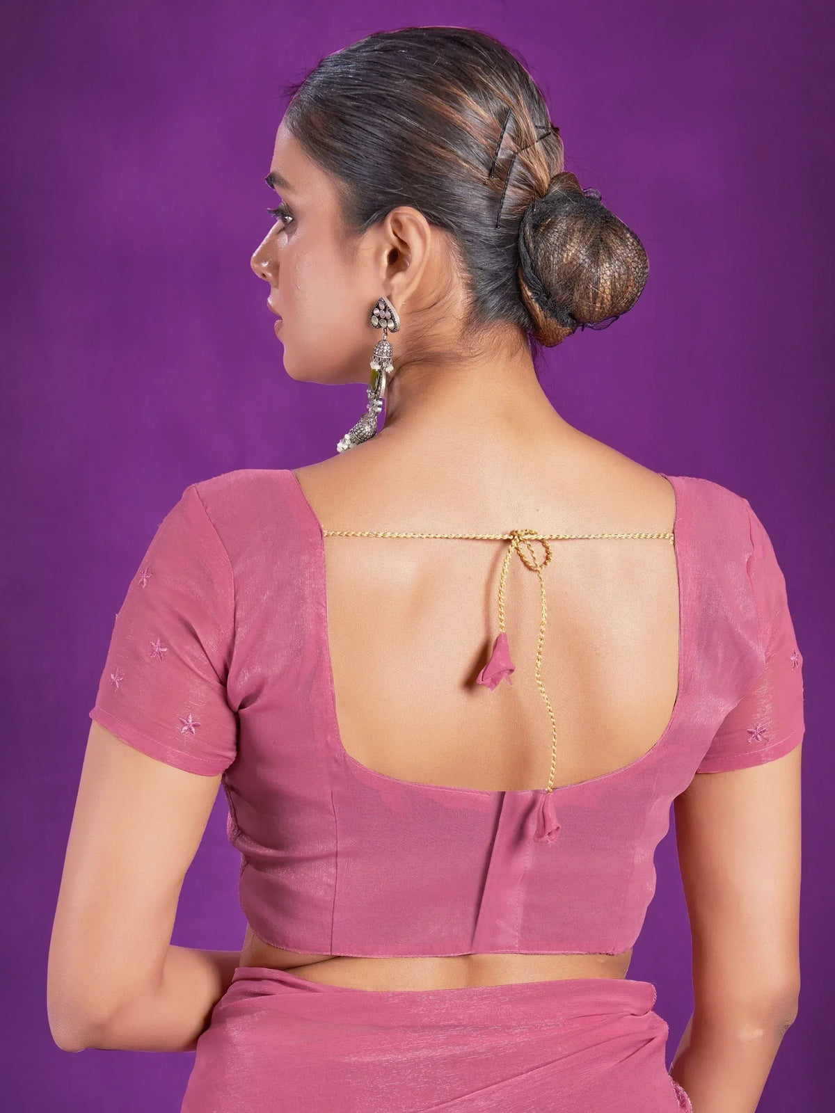 Pink saree blouse with open back, gold tie, and star embroidery, styled with traditional earrings