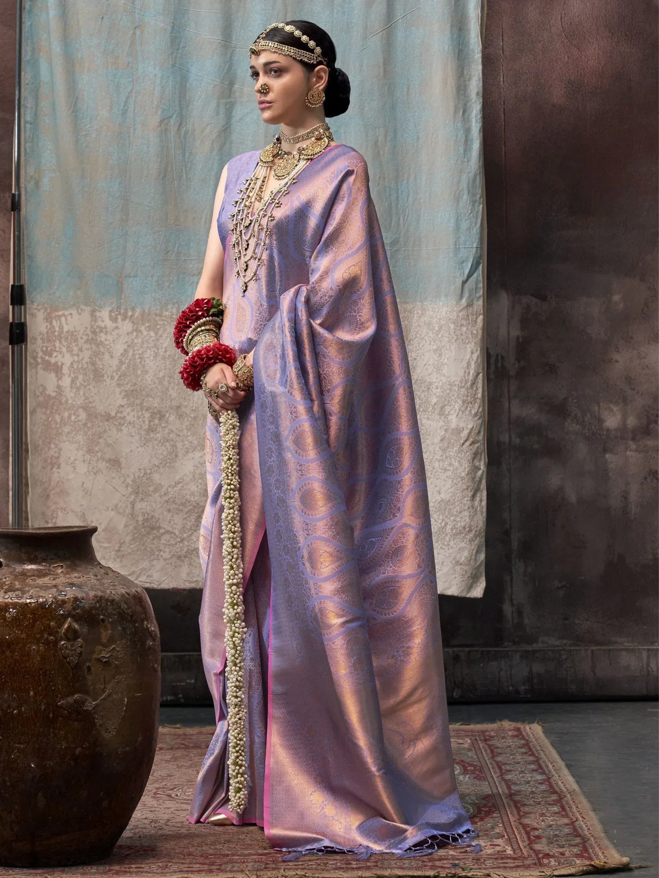 Woman in lavender silk saree with gold paisley print, traditional Indian jewelry, and floral garland